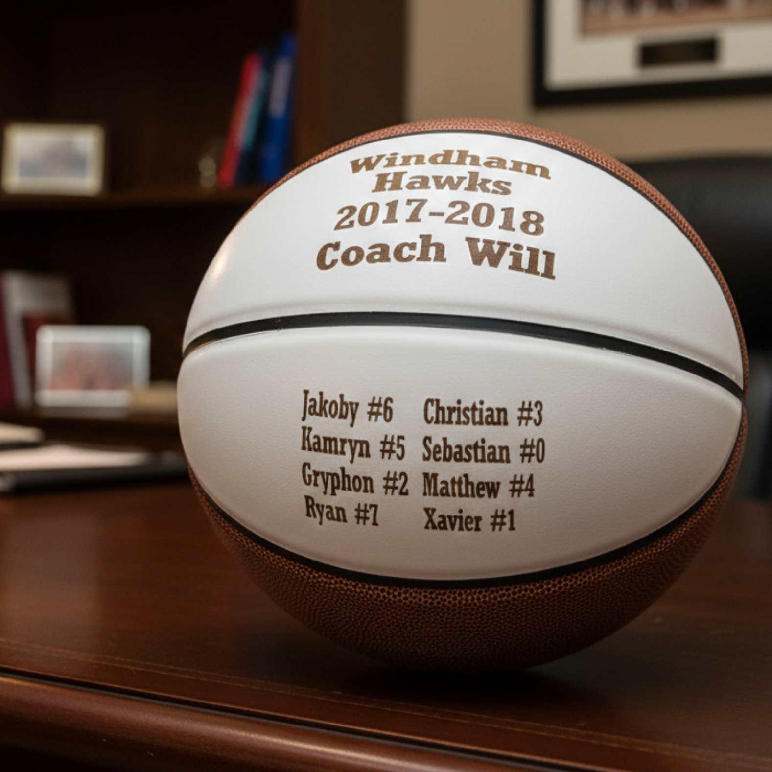Basketball engraved with sample text "Windham Hawks 2017-2018 Coach Will" and player roster with names and numbers on white panel.