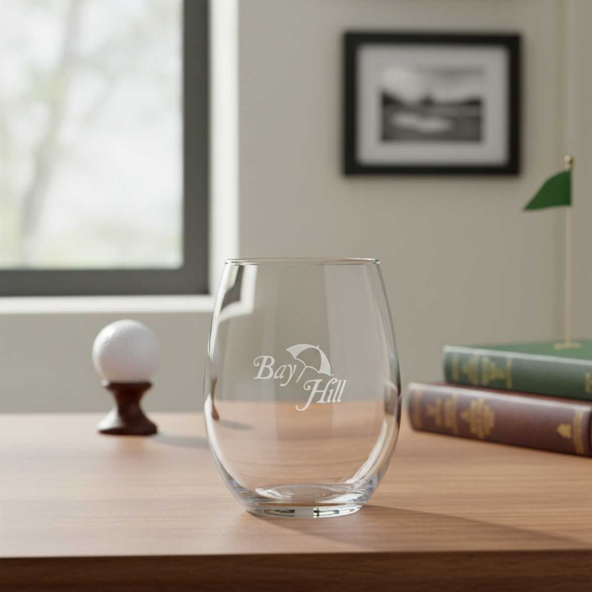 Stemless wine glass with a sample logo laser-engraved on the front, displayed on a wooden desk.