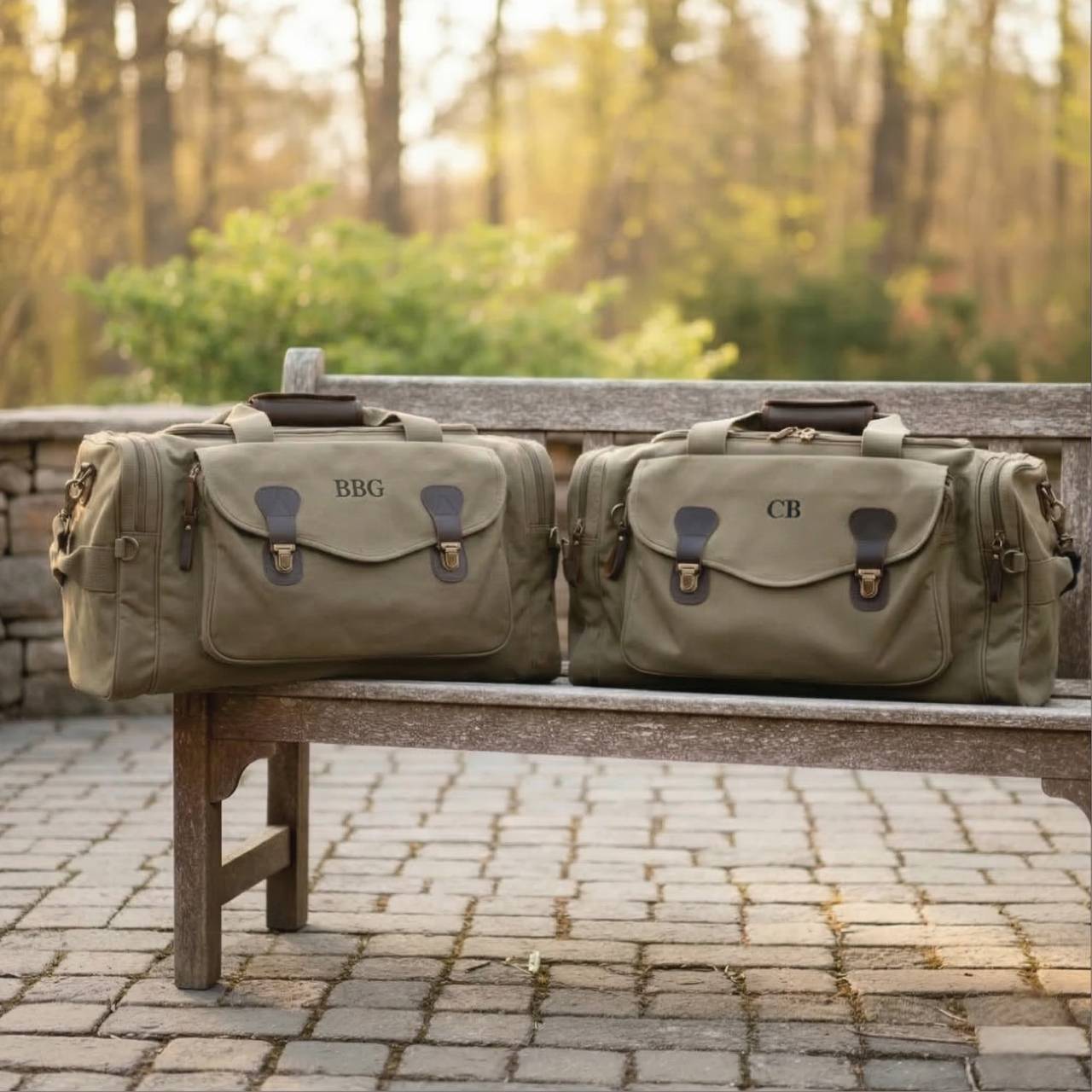 Two tan canvas weekender bags with leather accents displayed on a wooden bench, each personalized with sample monogram examples "BBG" and "CB