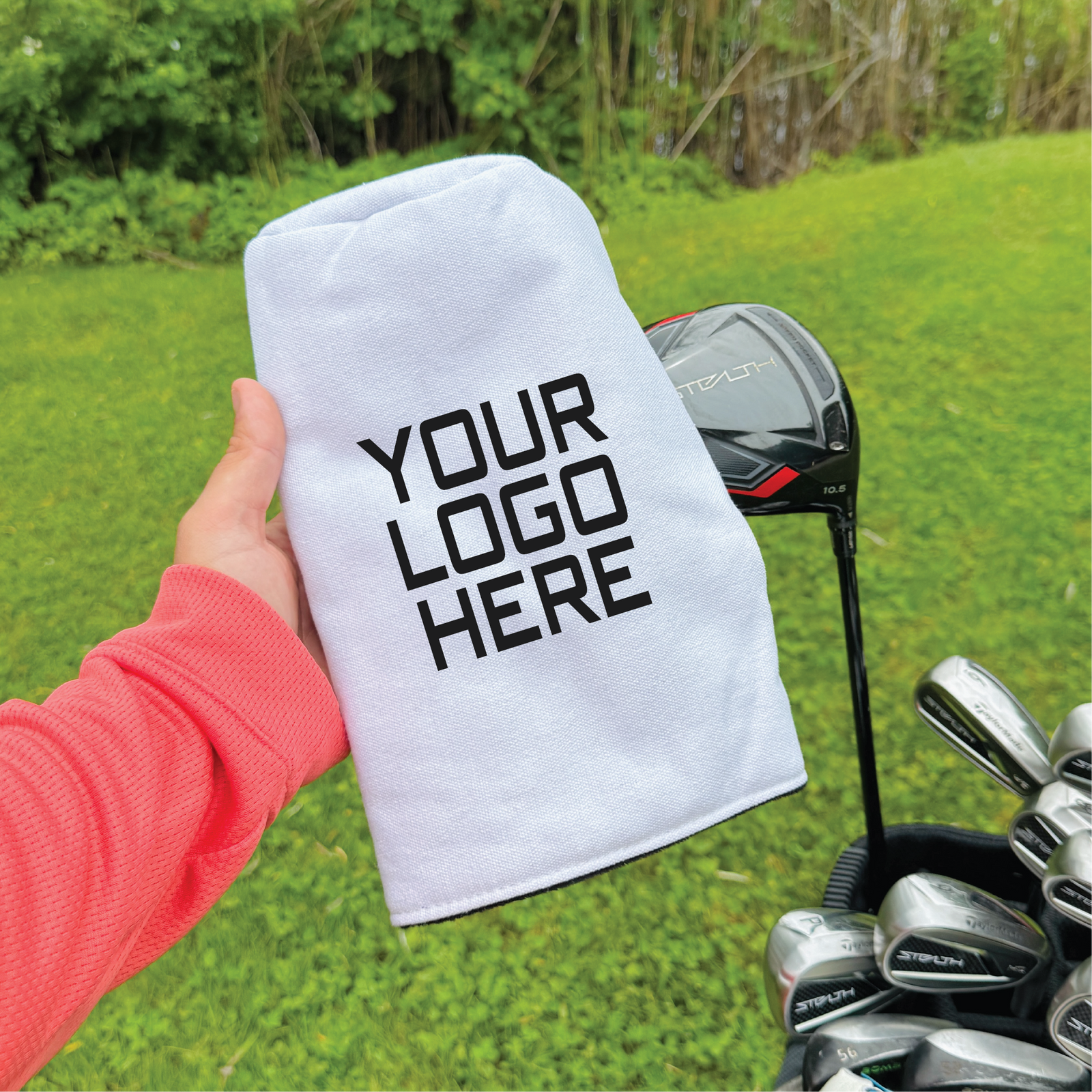 White golf club headcover with sample logo text held over golf bag on grass course
