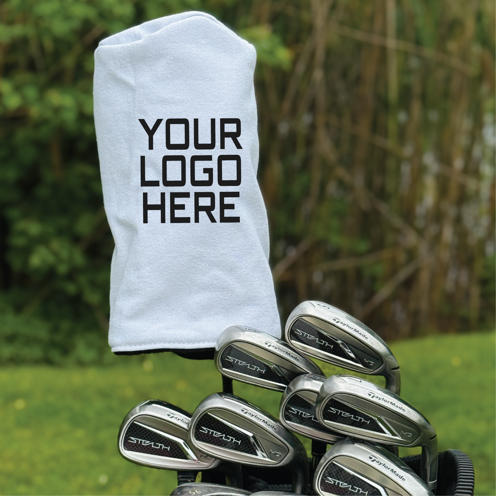 White barrel-shaped headcover with sample logo placeholder text displayed with golf irons on grass background