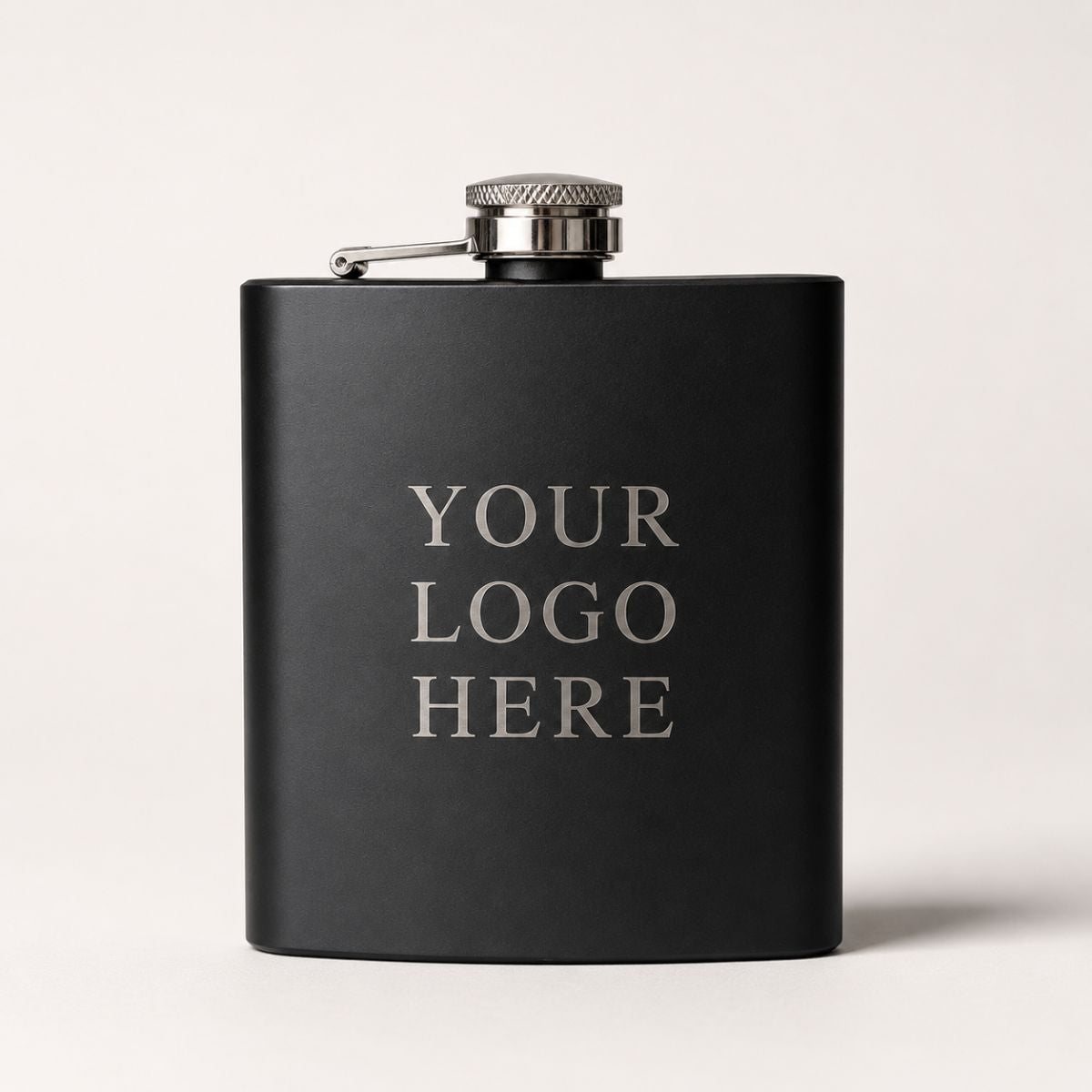 Matte black custom logo flask engraved with a Your Logo Here sample on a neutral wood desk, showing where a company logo is placed.