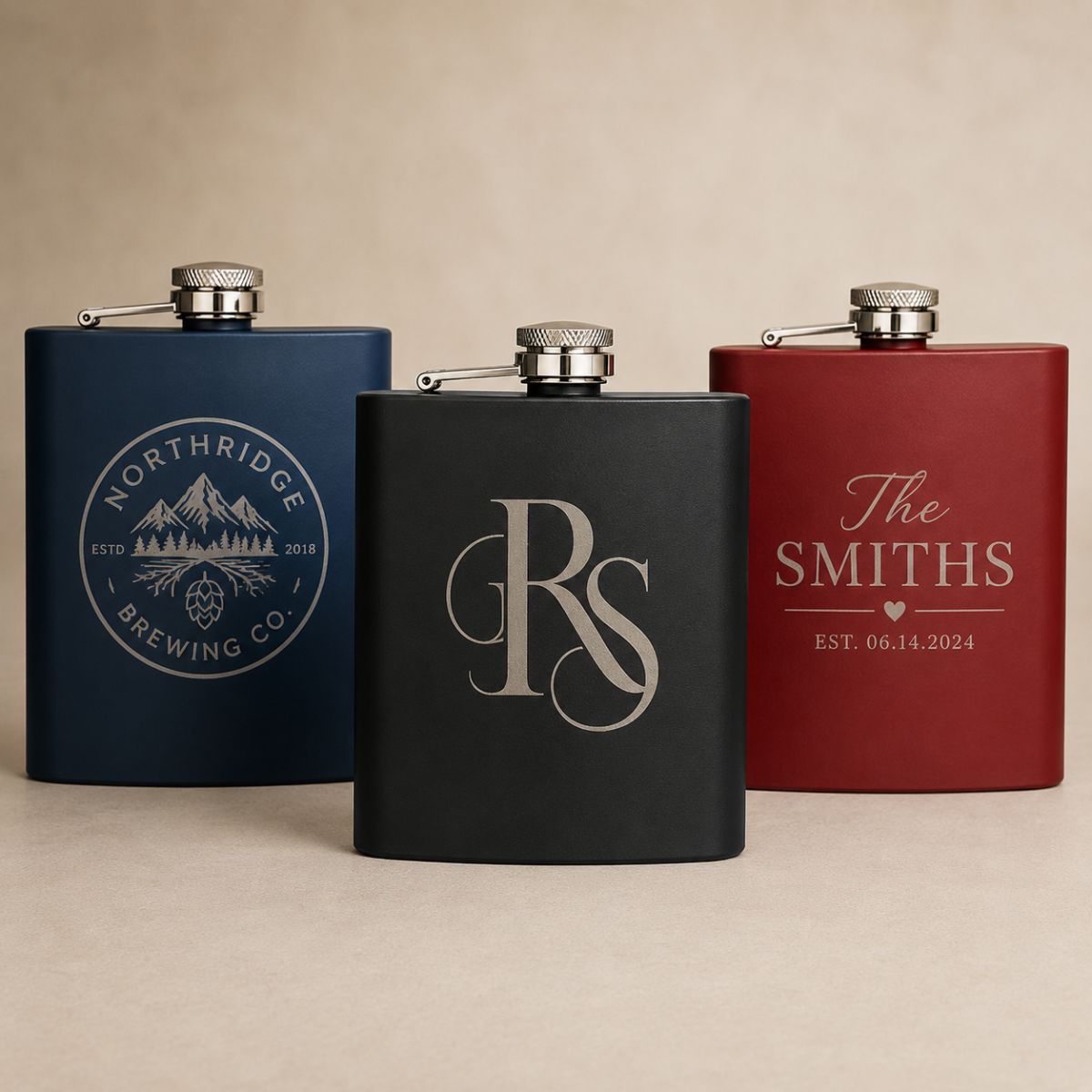Three custom logo flasks engraved with different sample company and monogram designs, showing the range of logos we can laser engrave.