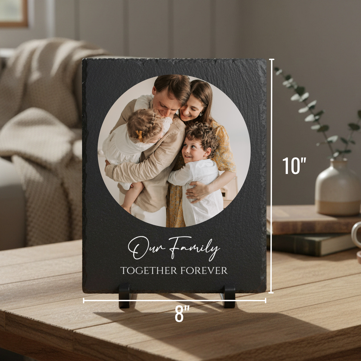 Black slate plaque with circular photo of family with two children, personalized with sample text "Our family Together Forever" displayed on wooden table with easel stand