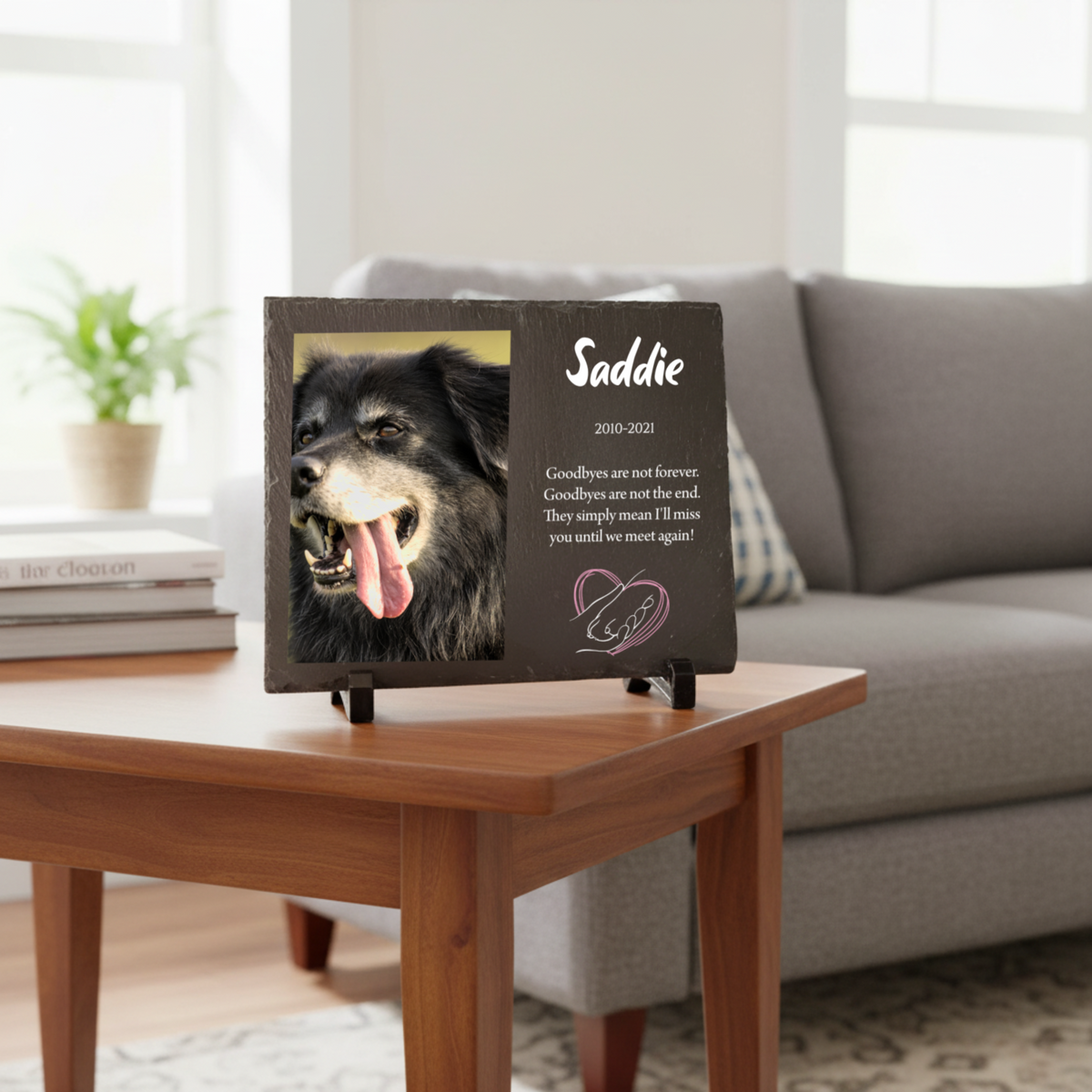 Dark slate memorial plaque with photo of dog named Saddie, dates 2010-2021, and personalized farewell message with heart design on wooden table