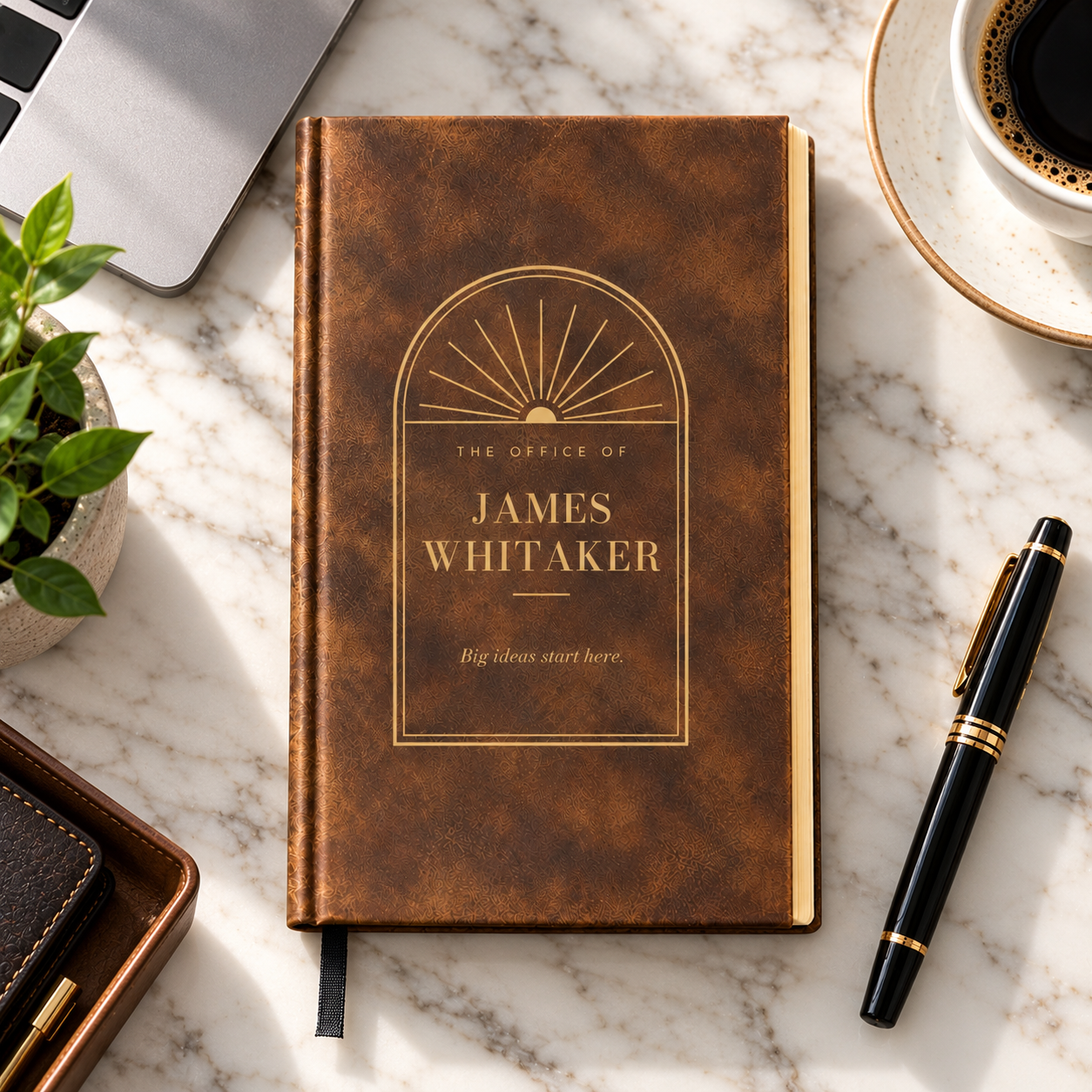 Personalized journal for men in brown, engraved in gold with The Office of James Whitaker inside an arched office door window, on an marble counter
