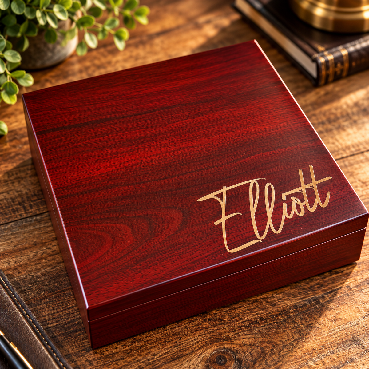 Red mahogany wood box with gold engraved name "Elliott" on lid, displayed on wooden table with books and greenery