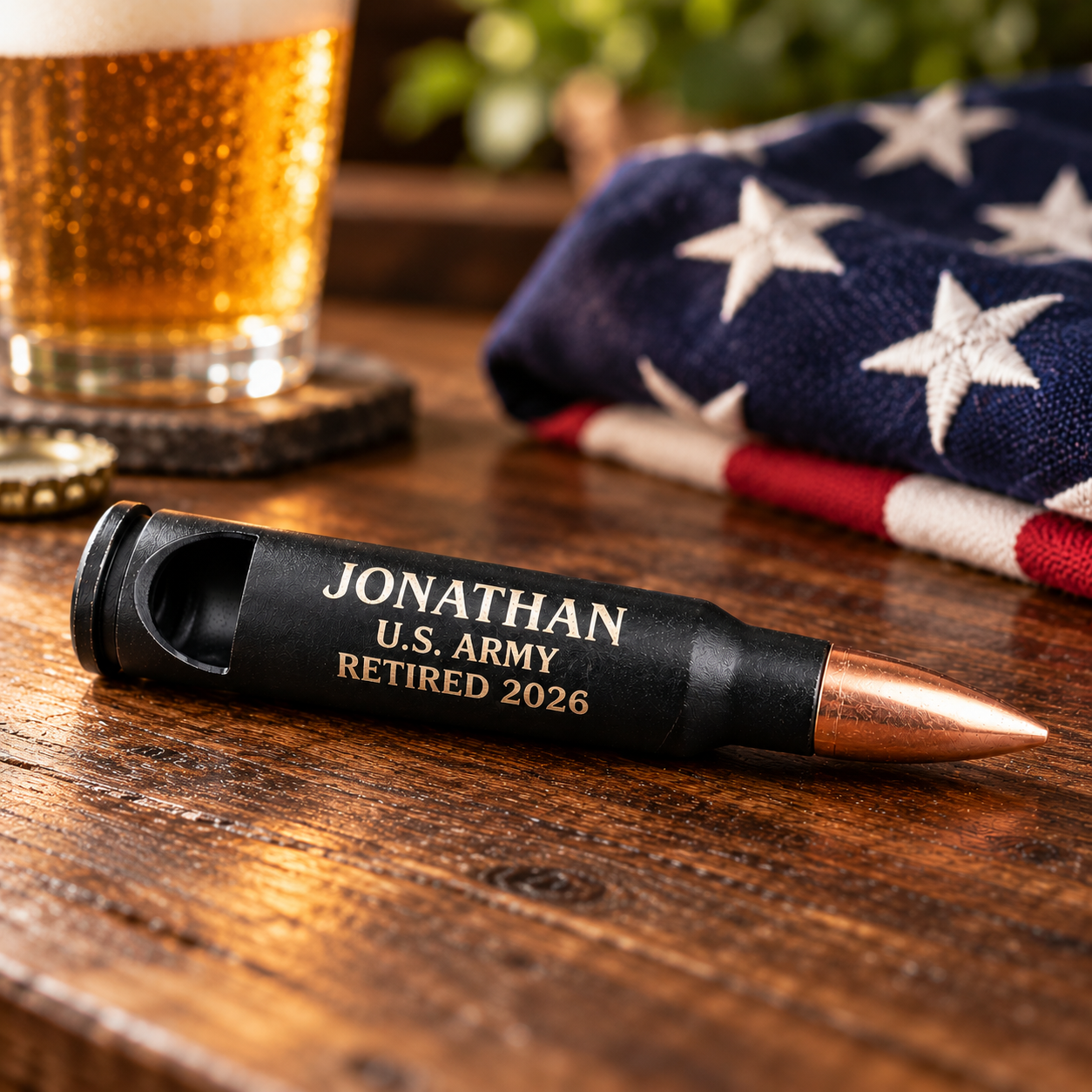 Engraved 50 cal bullet bottle opener in matte black with a copper tip, laser engraved Jonathan, U.S. Army, Retired 2026 on a bar top with American Flag folded and beer glass
