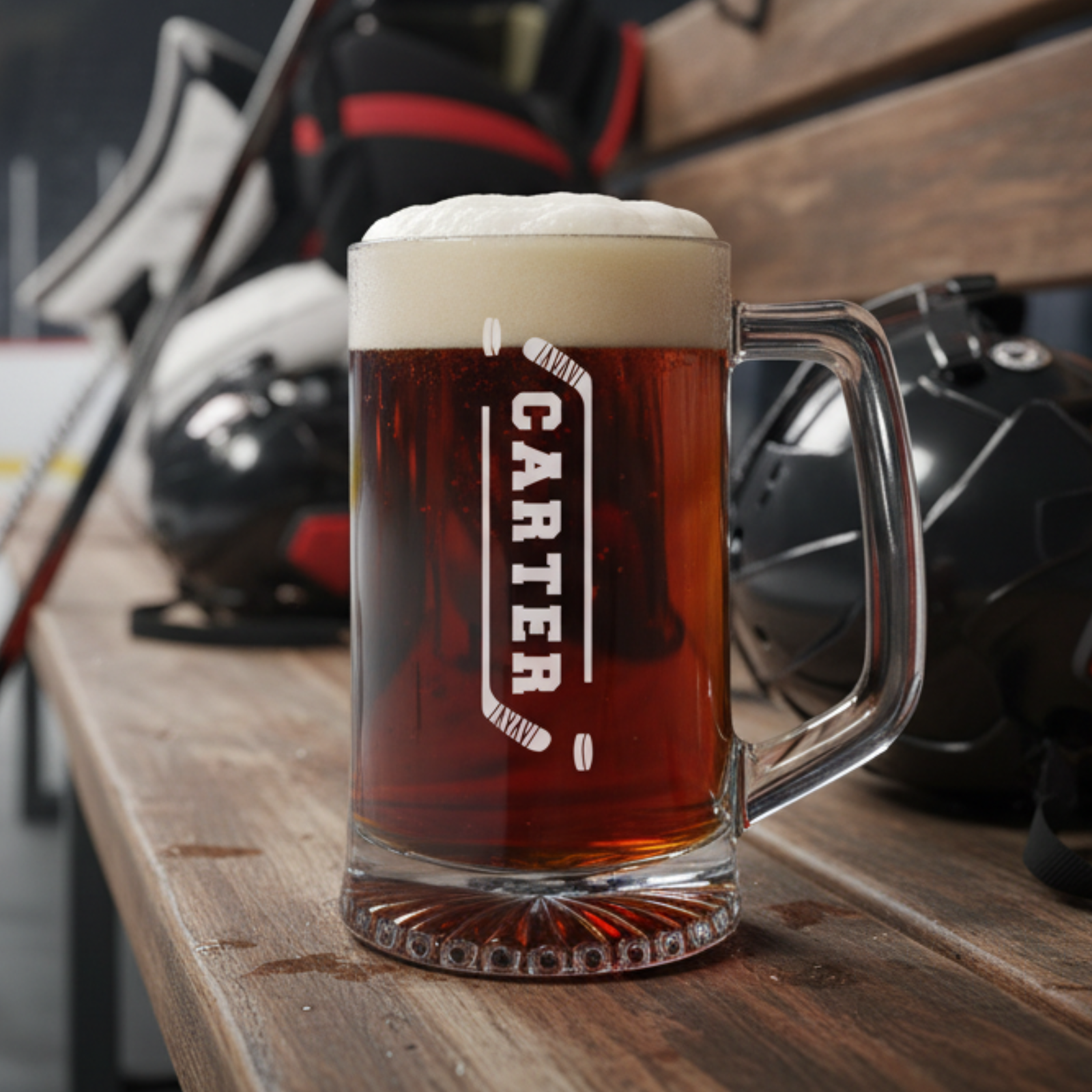 Beer mug filled with dark beer and foam head, etched with sample name "CARTER" flanked by crossed hockey stick designs, sitting on wooden surface with blurred hockey equipment in background