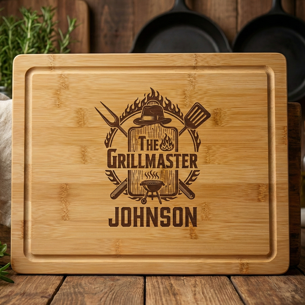 Bamboo cutting board laser-engraved with sample design "The Grill Master" title, crossed grilling tools, flame motif, and "JOHNSON" name personalization, featuring juice groove border