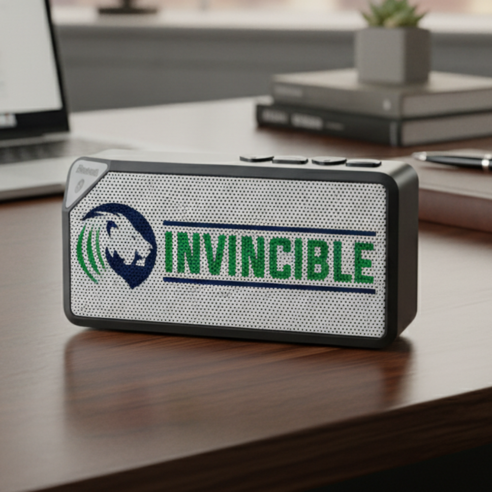 Portable speaker with custom company logo and text printed on mesh front panel, displayed on desktop.