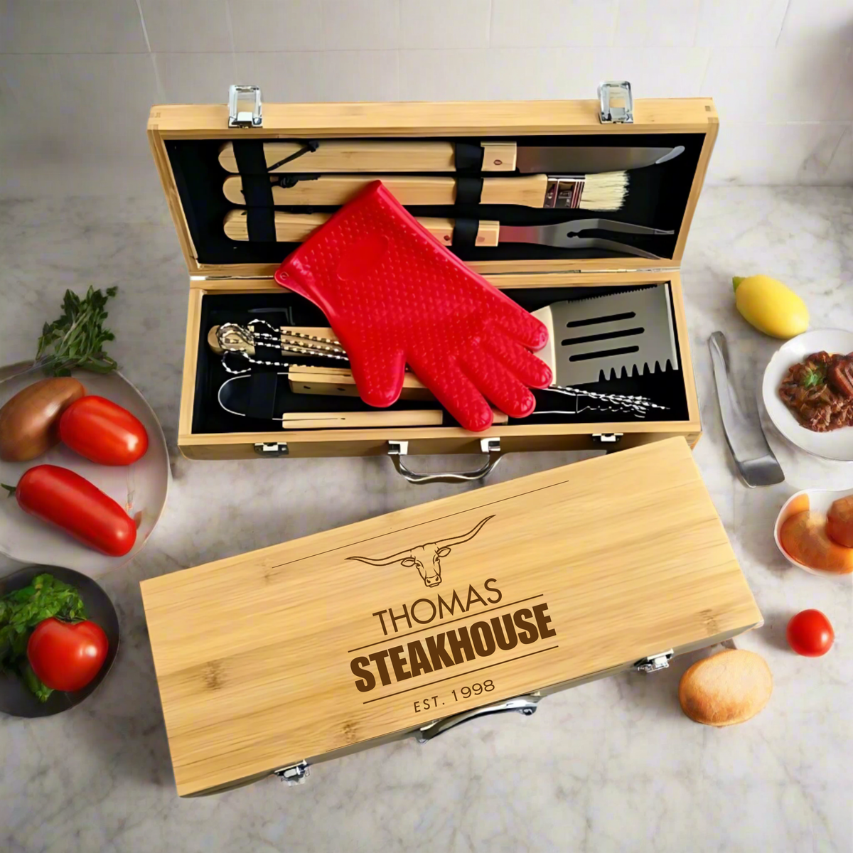Personalized bamboo grill tool set with engraved name "THOMAS" and "STEAKHOUSE EST. 1998", includes brushes, tongs, spatula, fork, and red gloves in wood case