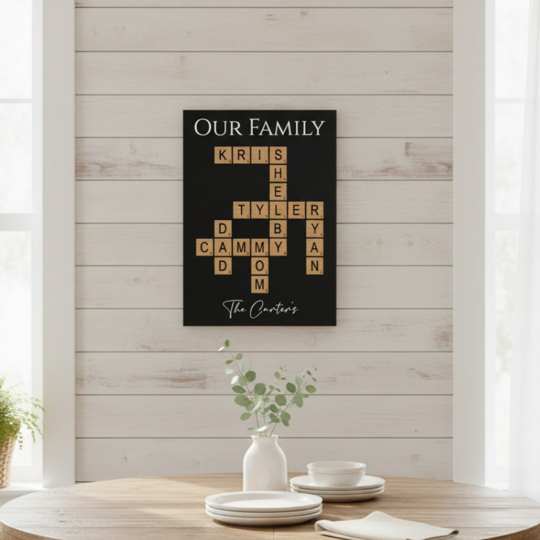 Black wall sign displayed above wooden table with sample family names arranged in crossword-puzzle style, personalized with "The Carters" at bottom