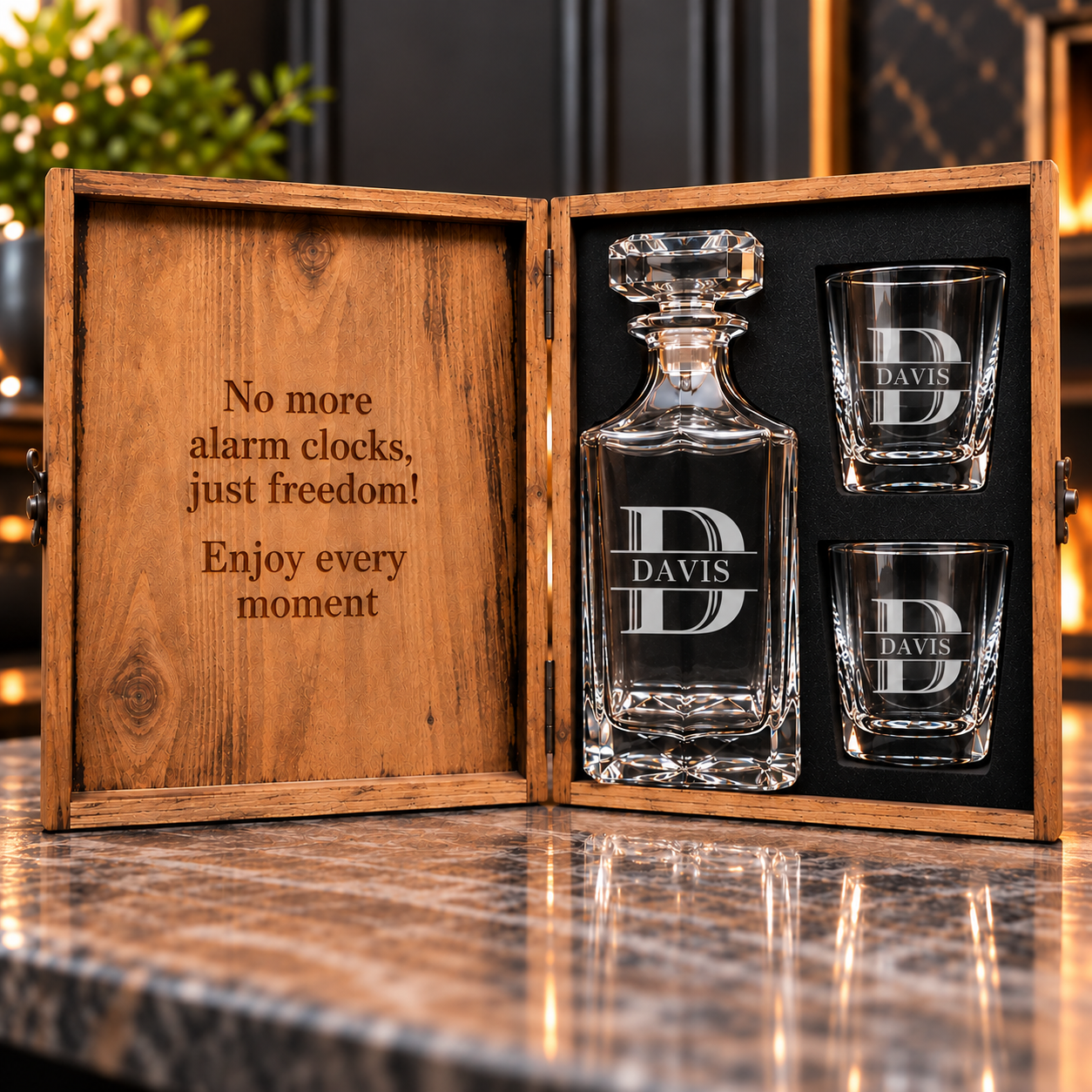 Personalized whiskey decanter and two matching shot glasses in an open wooden gift box, displayed on a polished marble countertop. The glassware is etched with a monogram 'D' and the name 'DAVIS', and the box interior is lined with black foam.