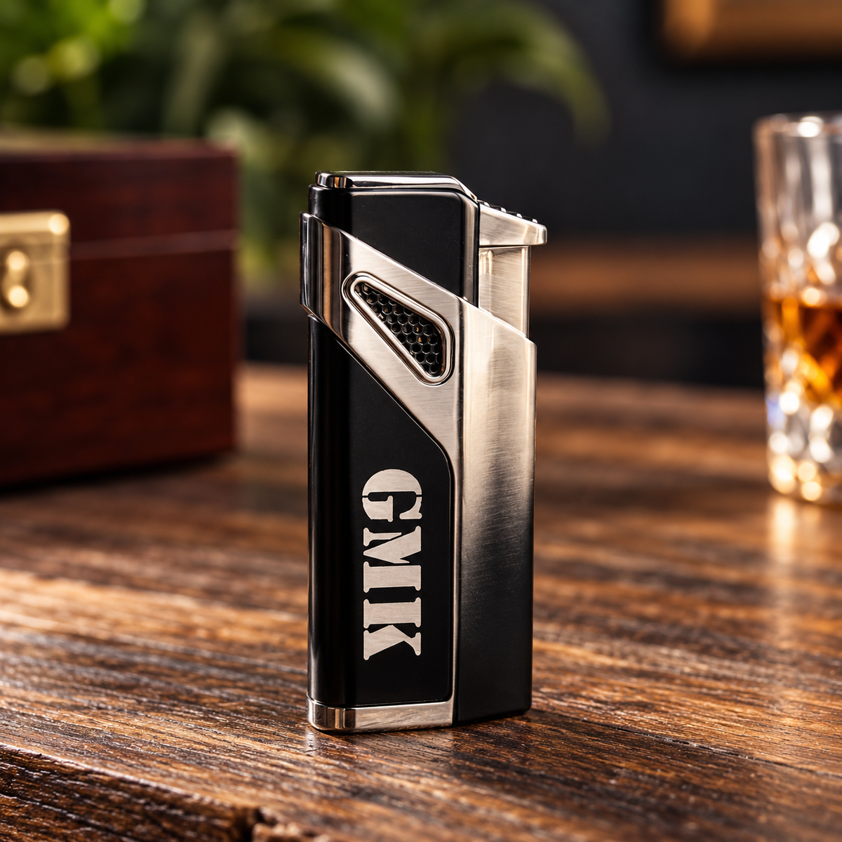 Stainless steel cigar cutter with black enamel panel and engraved monogram "CMK" on wooden desk with accessory box and whiskey glass