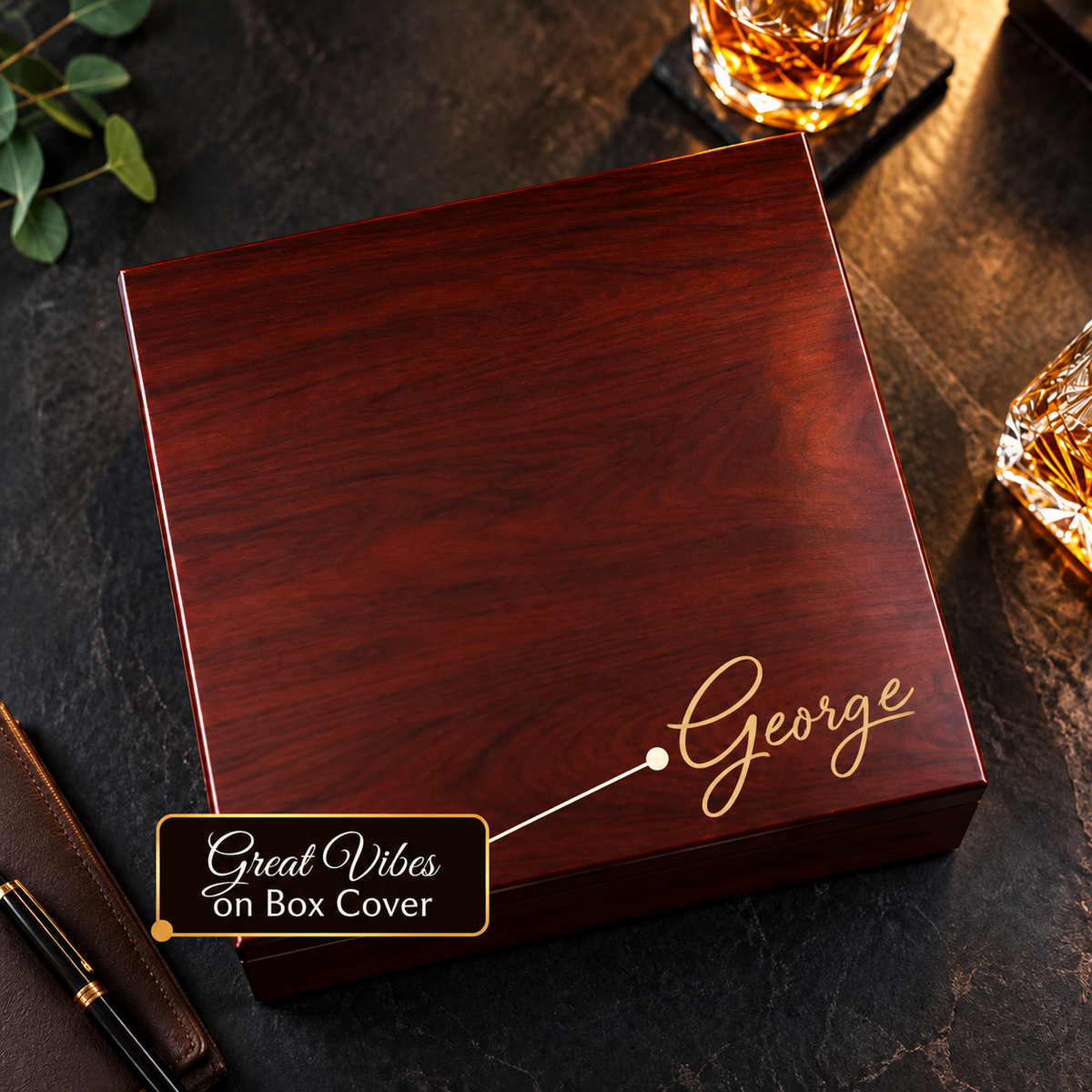 Closed cherry personalized keepsake box on dark slate with the name George engraved in Great Vibes script on the lid, crystal whiskey glasses nearby