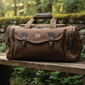 Custmized Brown duffel bag with 'RH' monogram on a bench in a forest setting
