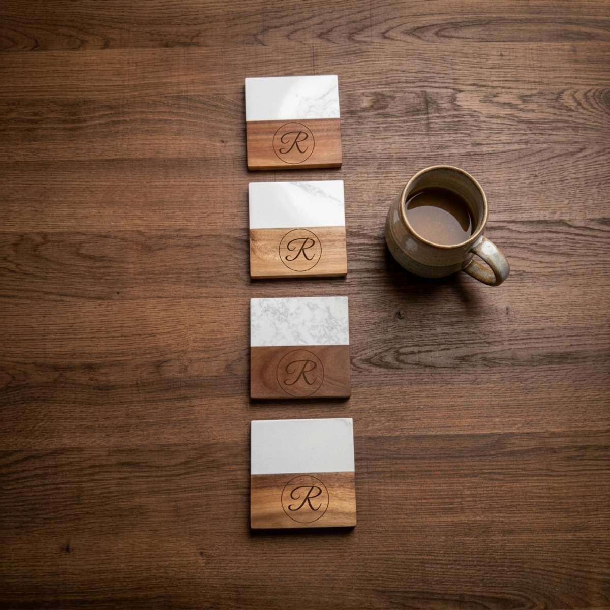 Four marble and acacia wood coasters engraved with a single monogram initial, stacked upright next to a ceramic mug on a wood surface.