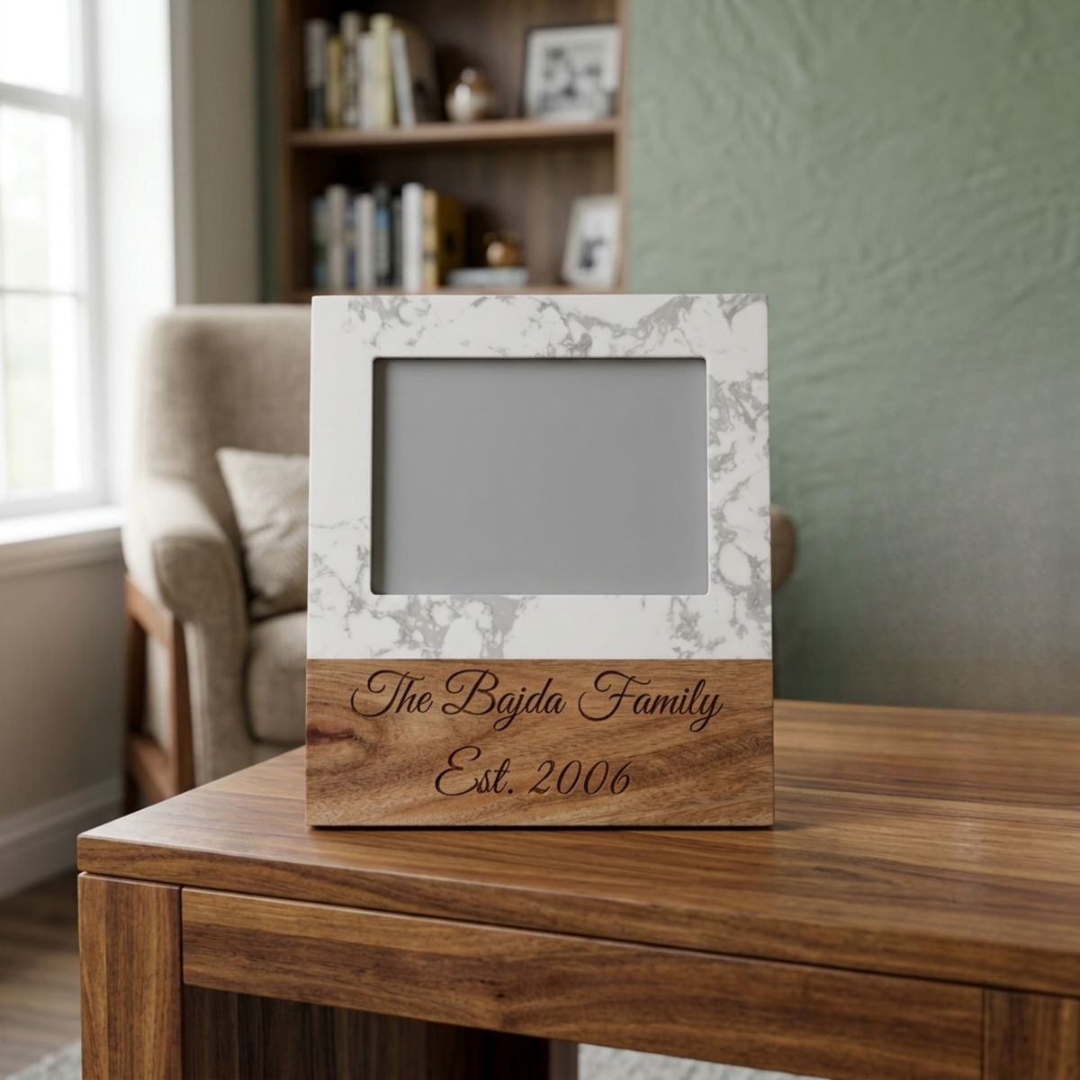 Marble and acacia wood picture frame engraved with a sample family name and established year, standing on a wood table beside a candle in a new home.