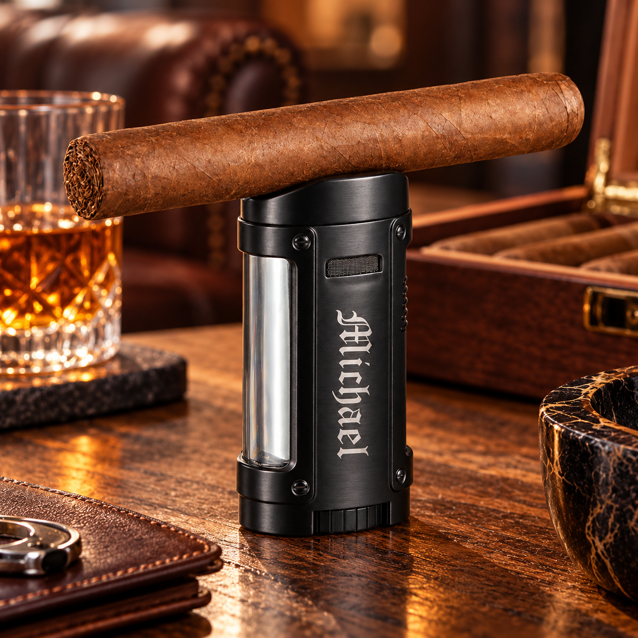 The Rhino quad torch cigar lighter in black, engraved Michael down the front, with a cigar resting on its cap, a luxury cigar lighter with whiskey glass and cigar box in background