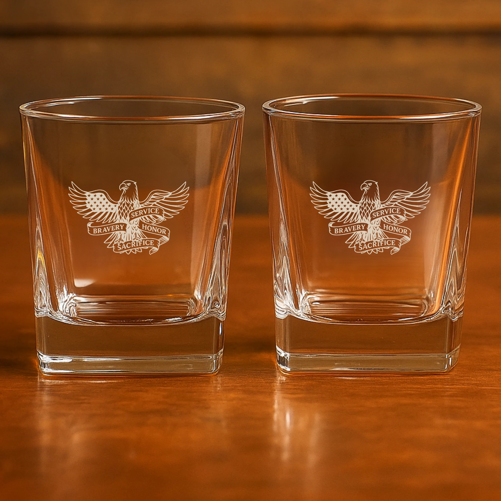 Pair of rocks glasses engraved with eagle and "Bravery Service Honor Sacrifice" emblem, displayed on wooden surface