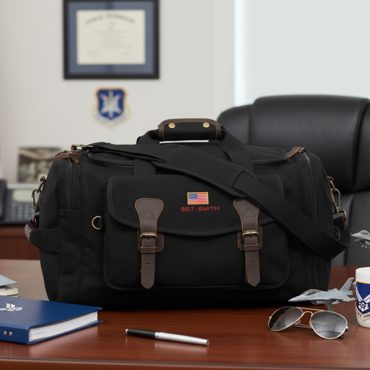Black canvas duffel with brown leather straps and brass hardware, personalized with sample embroidery reading "SGT. SMITH" and American flag on front panel
