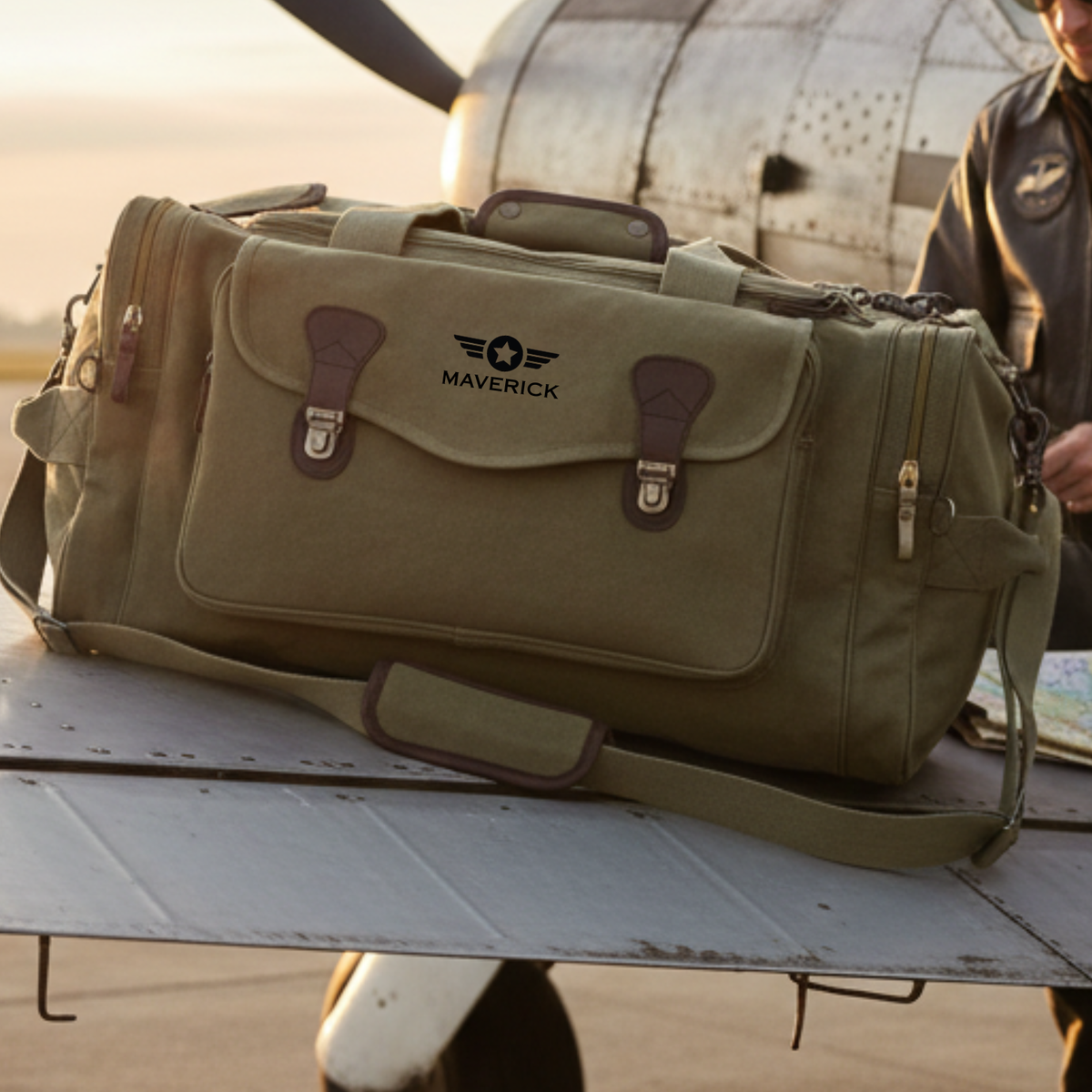 Tan canvas duffle bag with brown leather straps displayed on aircraft wing, featuring embroidered "MAVERICK" text and pilot wings logo