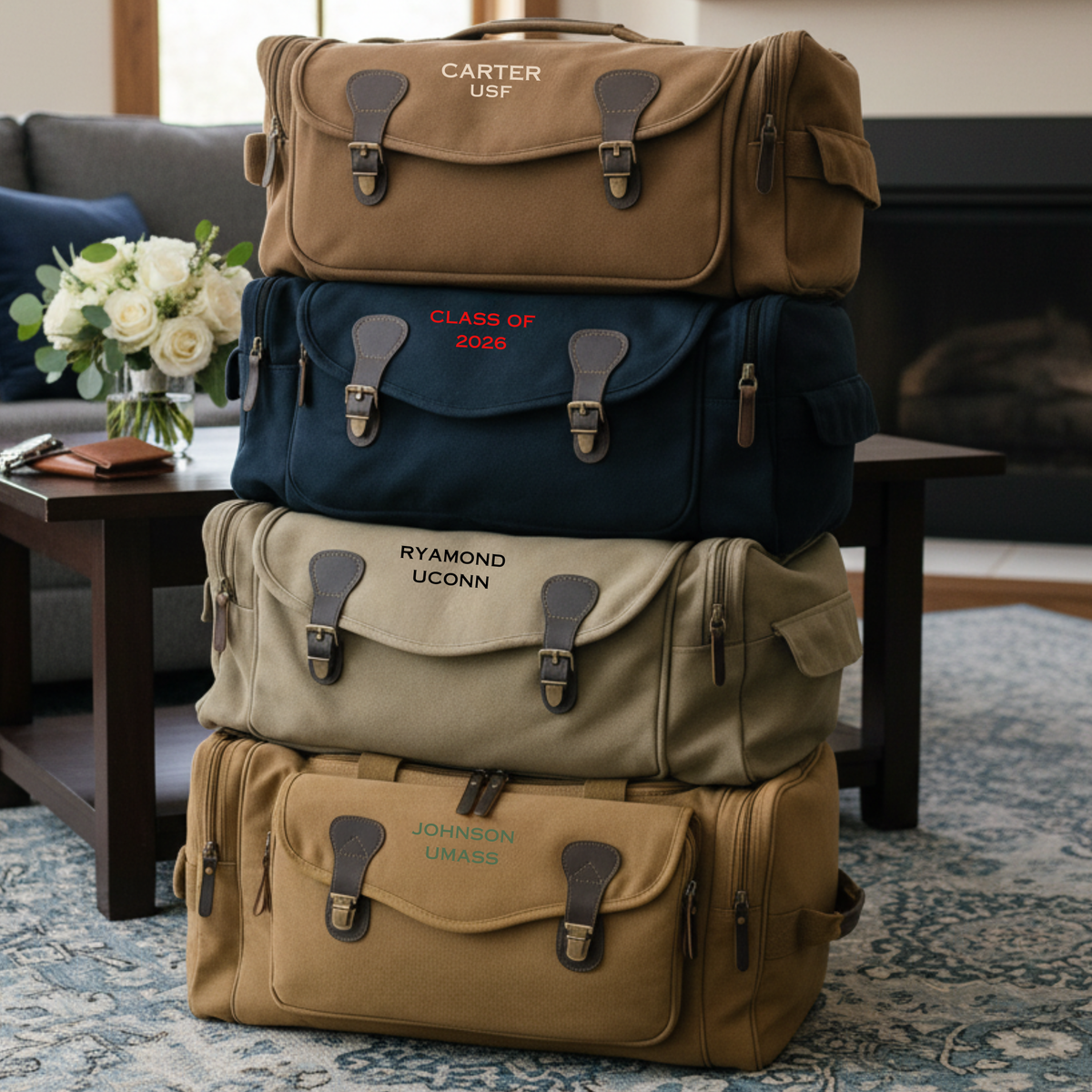 Four stacked personalized graduation duffle bags in tan, navy, khaki and camel, each embroidered with a graduate name and college.