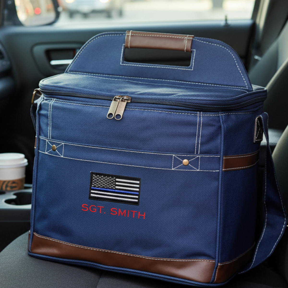 Navy canvas cooler with brown leather trim and handles, embroidered with thin blue line flag and sample text "SGT. SMITH", displayed in vehicle interior.