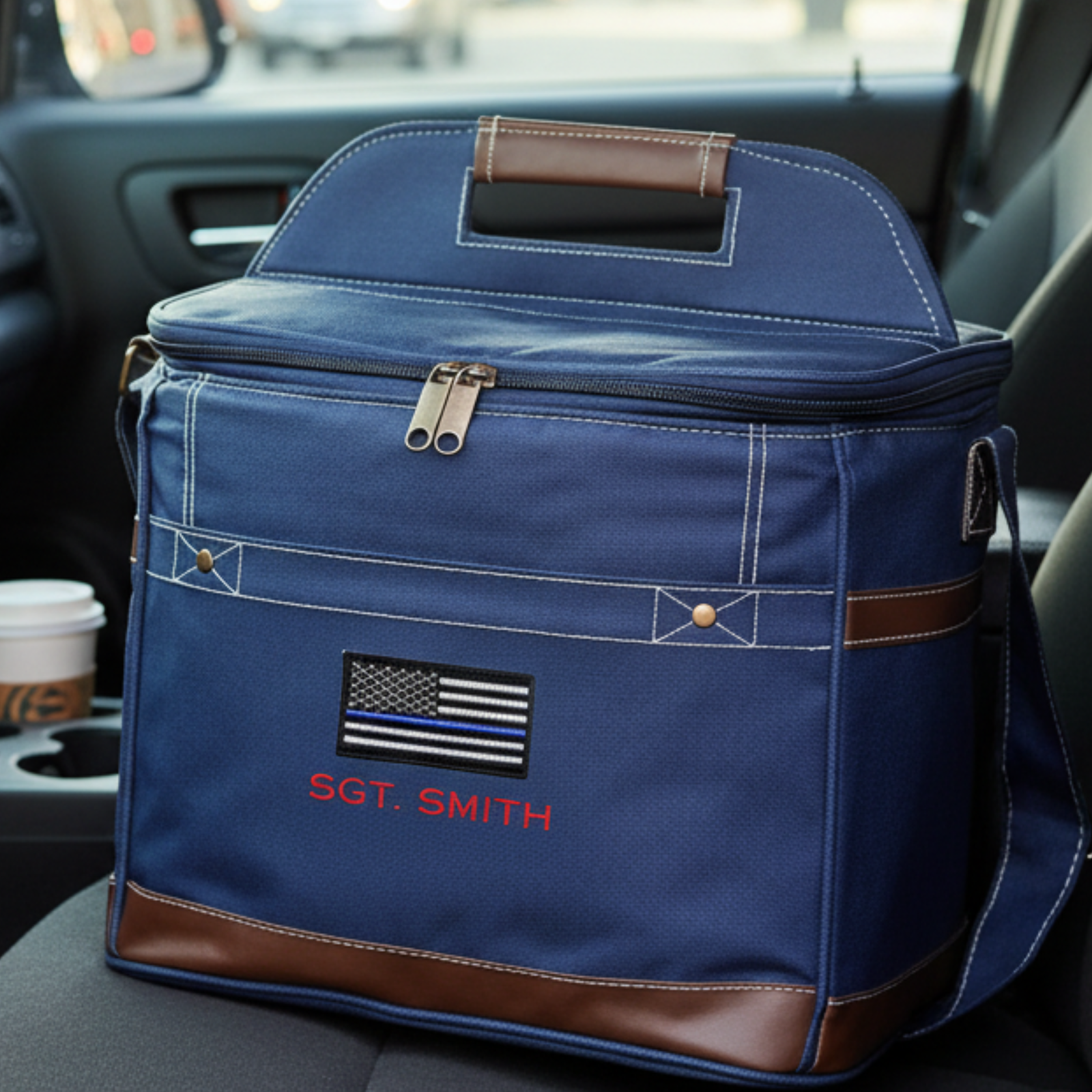 Navy canvas cooler with brown leather trim and handles, embroidered with thin blue line flag and sample text "SGT. SMITH", displayed in vehicle interior.