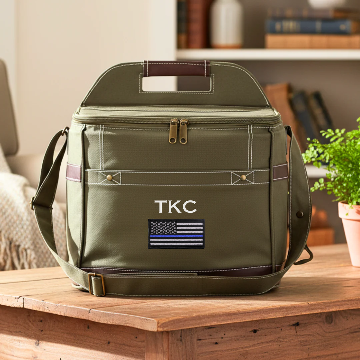 Olive canvas cooler with sample initials "TKC" and thin blue line flag emblem on front, brown leather handles and shoulder strap