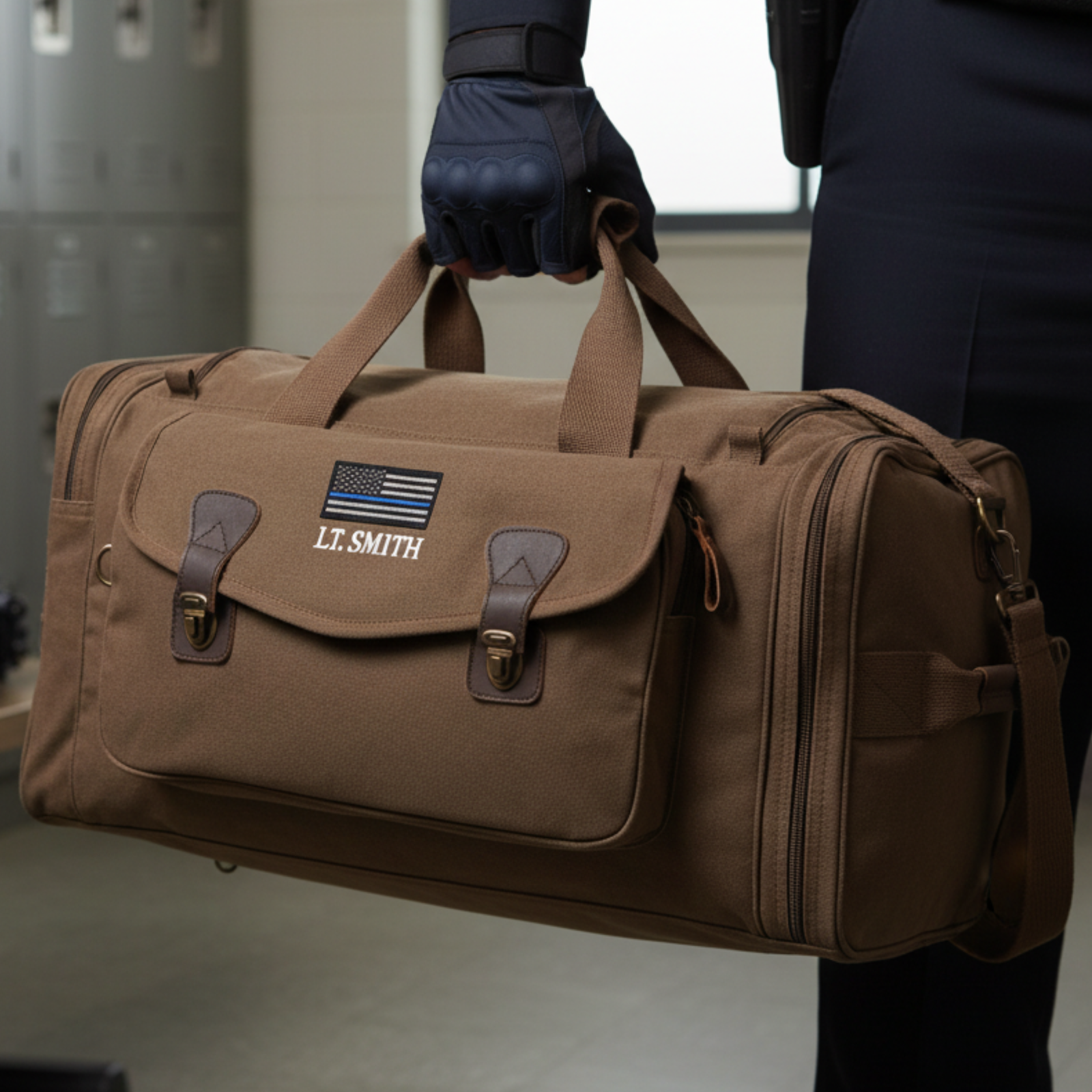 Tan canvas duffle bag with brown leather accents, personalized with sample name "LT. SMITH" and blue Thin Line flag patch, held by person wearing dark gloves and navy jacket