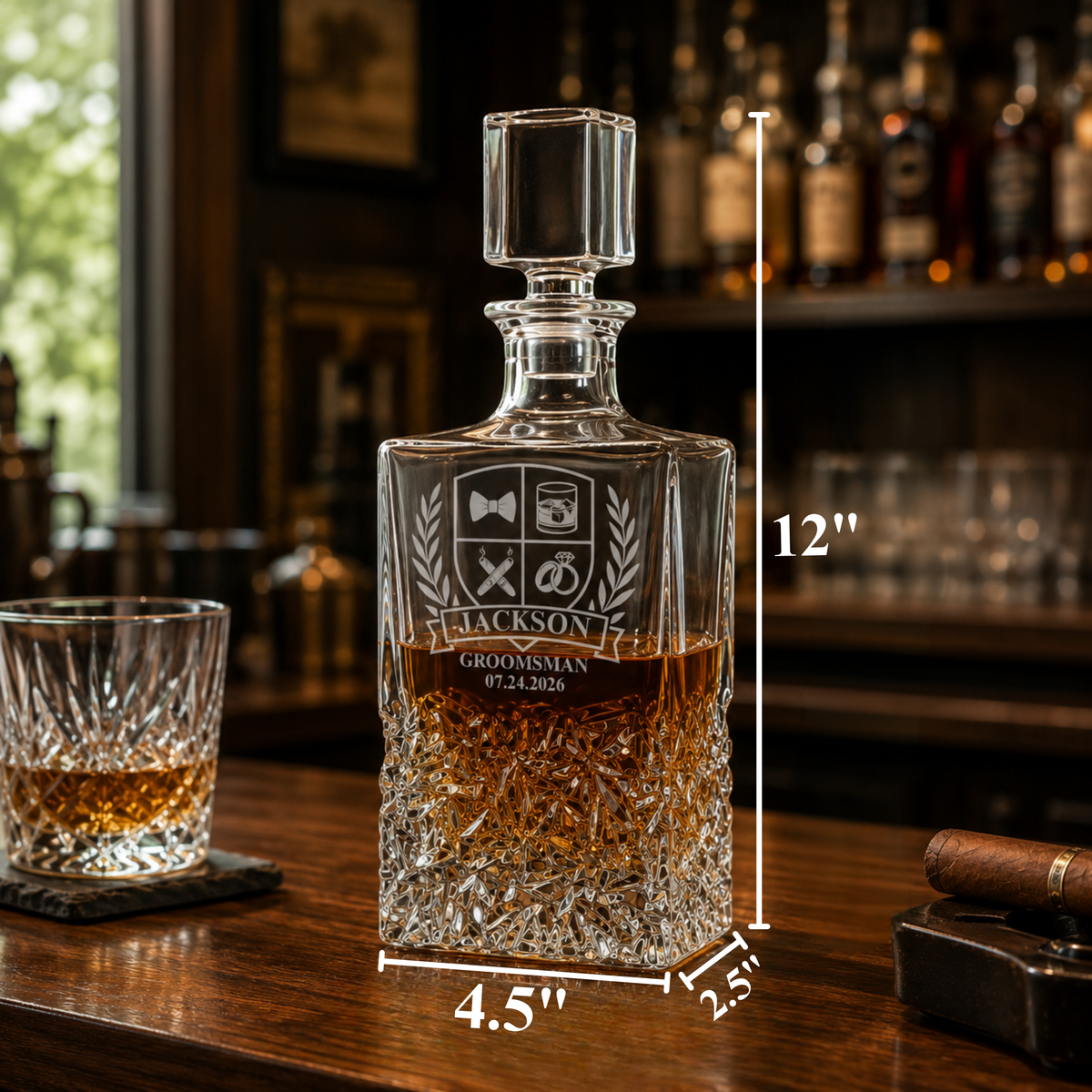 Engraved crystal decanter with sample personalization showing "Jackson Groomsman 07.24.2026" and decorative crest, displayed on wooden surface with whiskey glass and cigar.