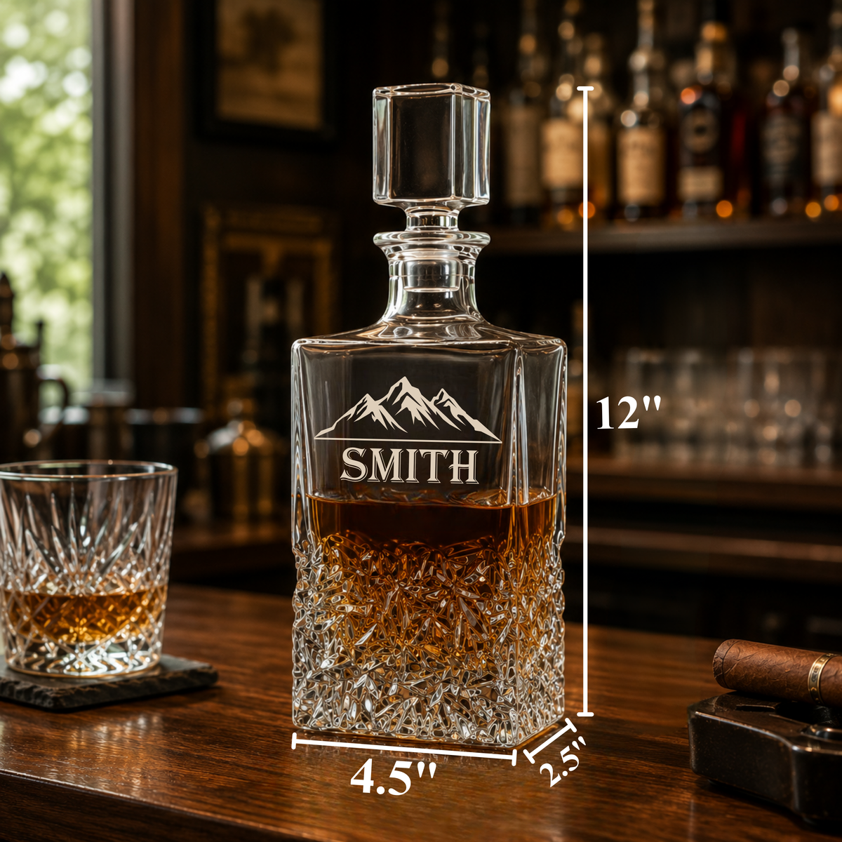 Crystal whiskey decanter with "SMITH" engraved sample and mountain design, 12 inches tall, shown with matching glass and cigar on wood bar.