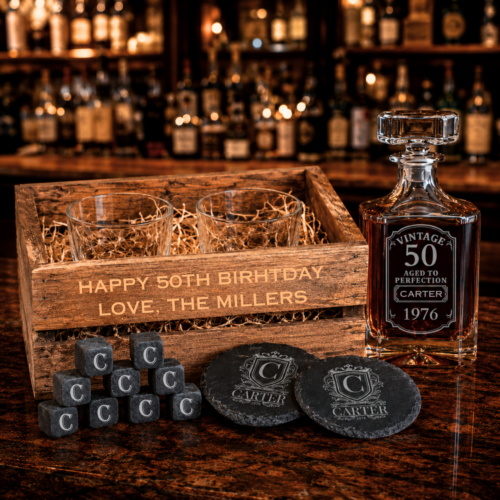 Engraved wooden crate with two whiskey glasses, crystal decanter with sample "Vintage 50" and "Carter" engraving, slate coasters, and monogrammed whiskey stones displayed on wood surface.