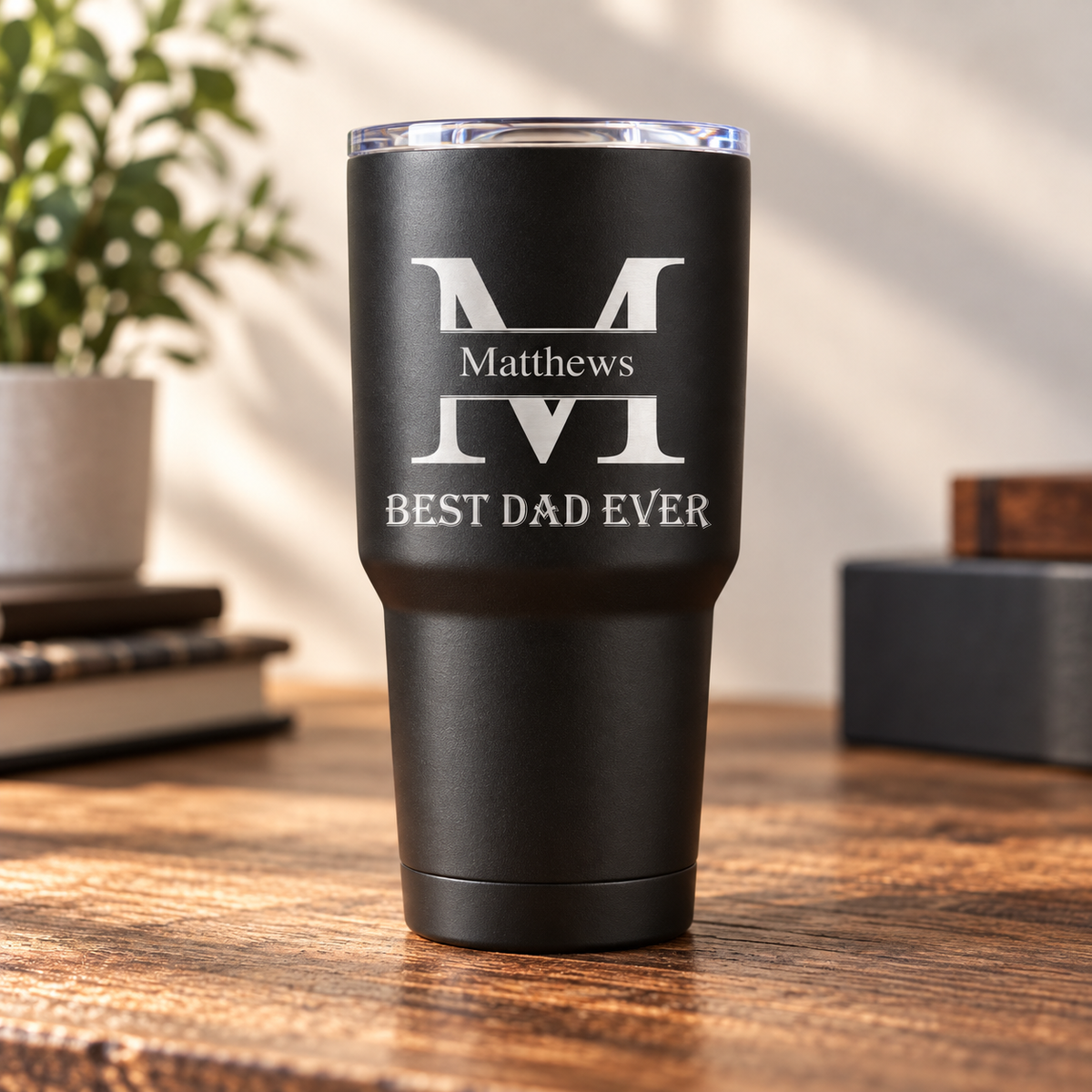 Black insulated tumbler with engraved monogram "M" and "Matthews" name with "BEST DAD EVER" text below, stainless steel rim, on wooden surface