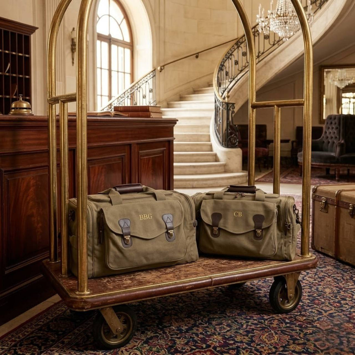 Two canvas weekender bags with leather accents displayed on vintage luggage cart, featuring sample monograms "BBG" and "CB" embroidered on front flaps