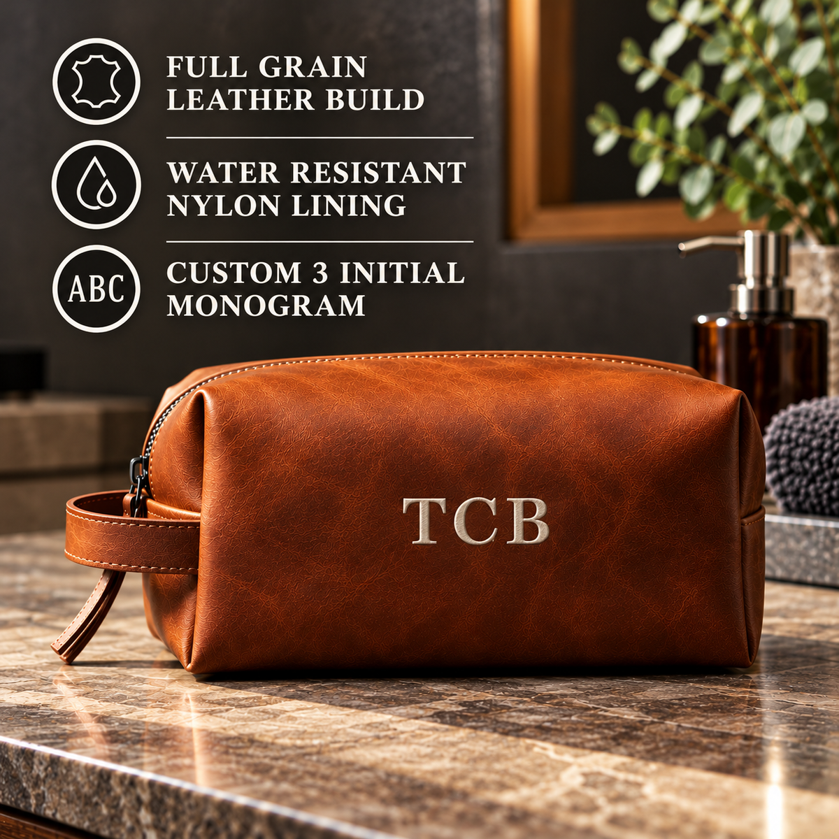 Cognac full-grain leather toiletry bag with sample monogram "CJB" embroidered on front, shown on wooden surface with feature callouts listing leather build, nylon lining, and customization options