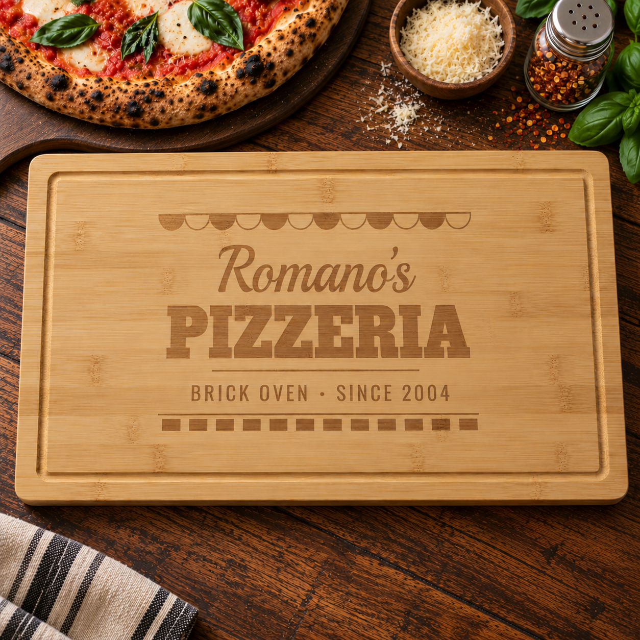 Personalized pizza cutting board engraved like a pizzeria sign, Romano's PIZZERIA BRICK OVEN SINCE 2004, beside a margherita pizza and parmesan