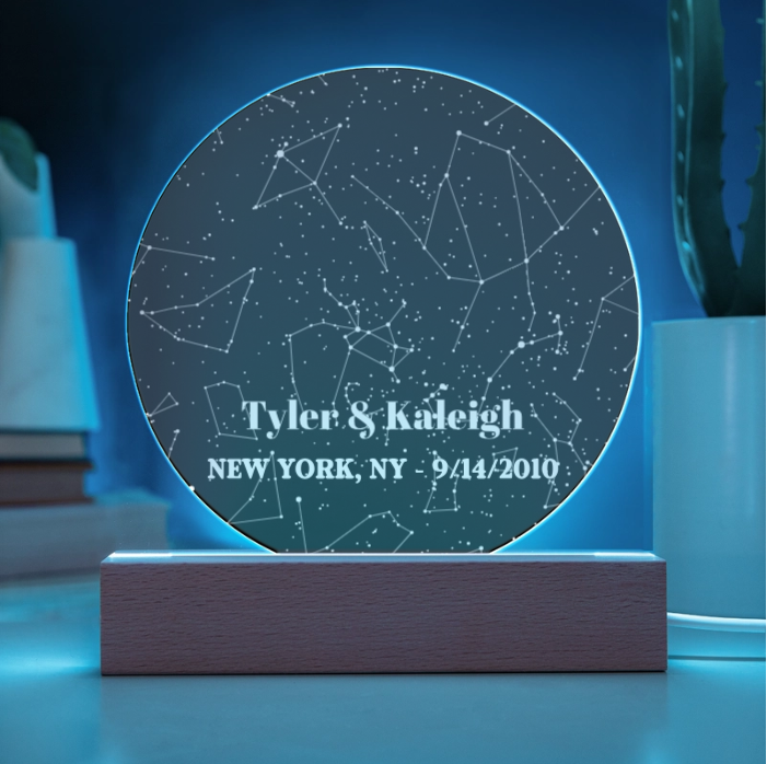 Round acrylic star map plaque with sample personalization "Tyler & Kaleigh, NEW YORK, NY - 9/14/2010" laser-engraved with constellation design, mounted on dark wood base with glowing blue LED light