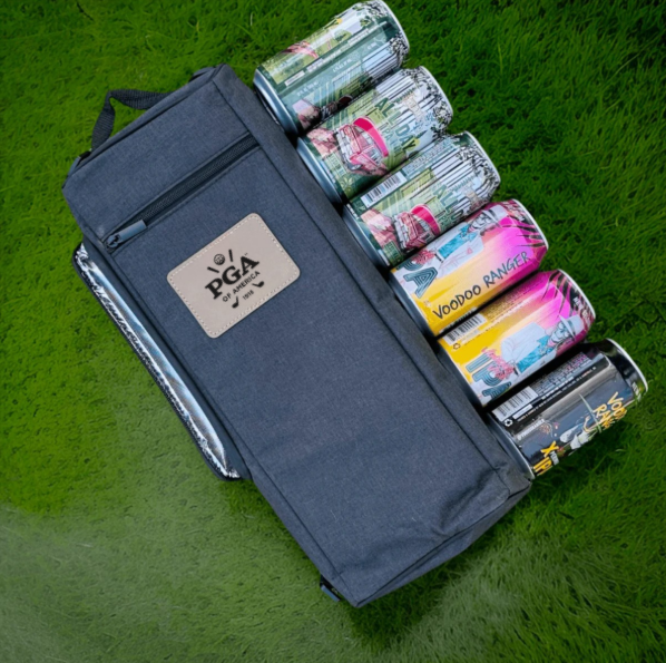 Navy cooler bag with branded logo patch displayed open on grass, revealing stacked beverage cans and drink packaging inside compartments