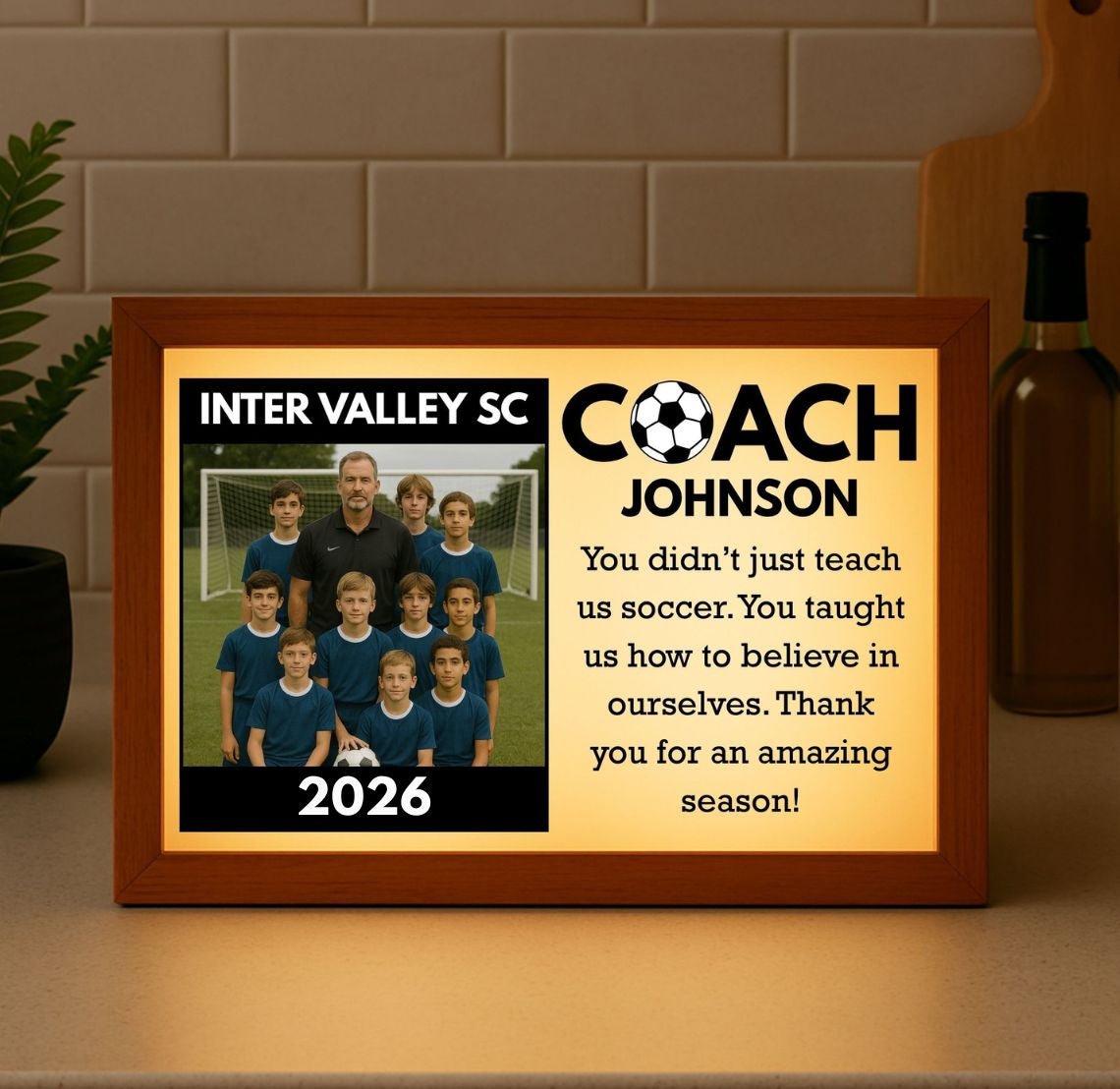Wood-framed light box with warm backlight displaying sample soccer team photo, "Inter Valley SC Coach Johnson" text, year 2026, and personalized thank you message on cream background