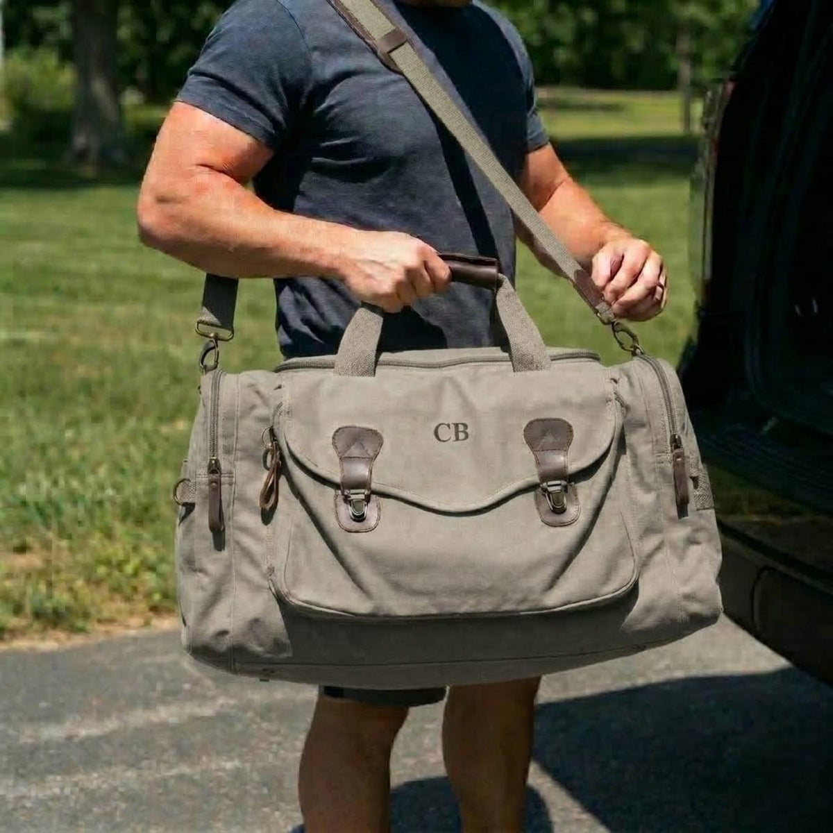 Tan canvas weekender bag with leather accents worn over shoulder, personalized with sample initials "CB" on front flap