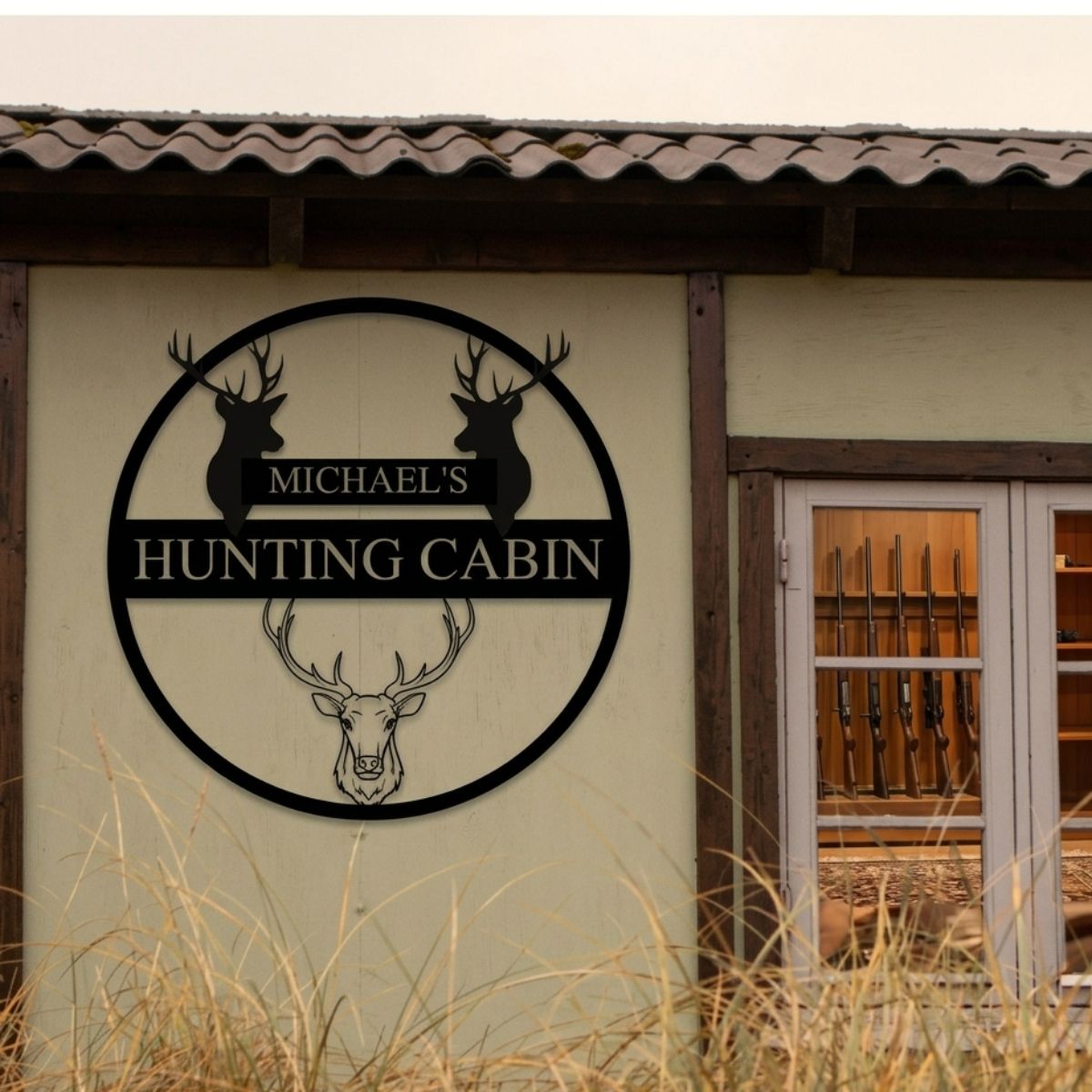 Black metal circular wall sign with deer silhouettes and sample personalization reading "Michael's Hunting Cabin" mounted on tan cabin exterior