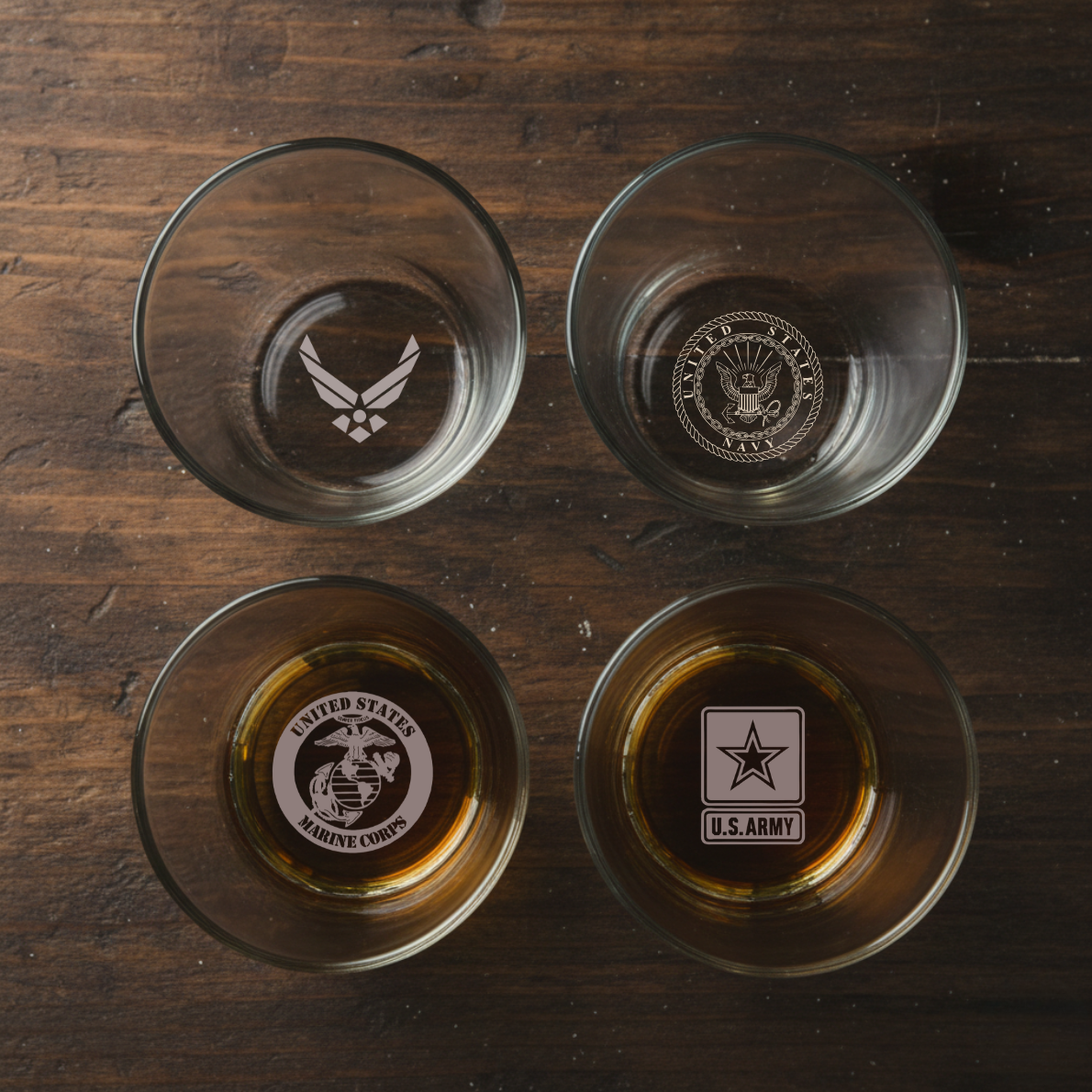 Four engraved whiskey glasses on wooden surface featuring Air Force, Navy, Marine Corps, and Army military branch emblems and seals.