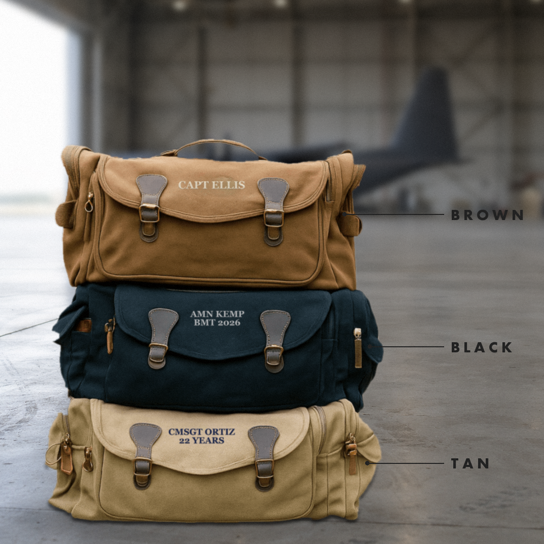 Brown, black and tan personalized canvas duffle bags stacked in an aircraft hangar, embroidered CAPT ELLIS, AMN KEMP BMT 2026 and CMSGT ORTIZ 22 YEARS