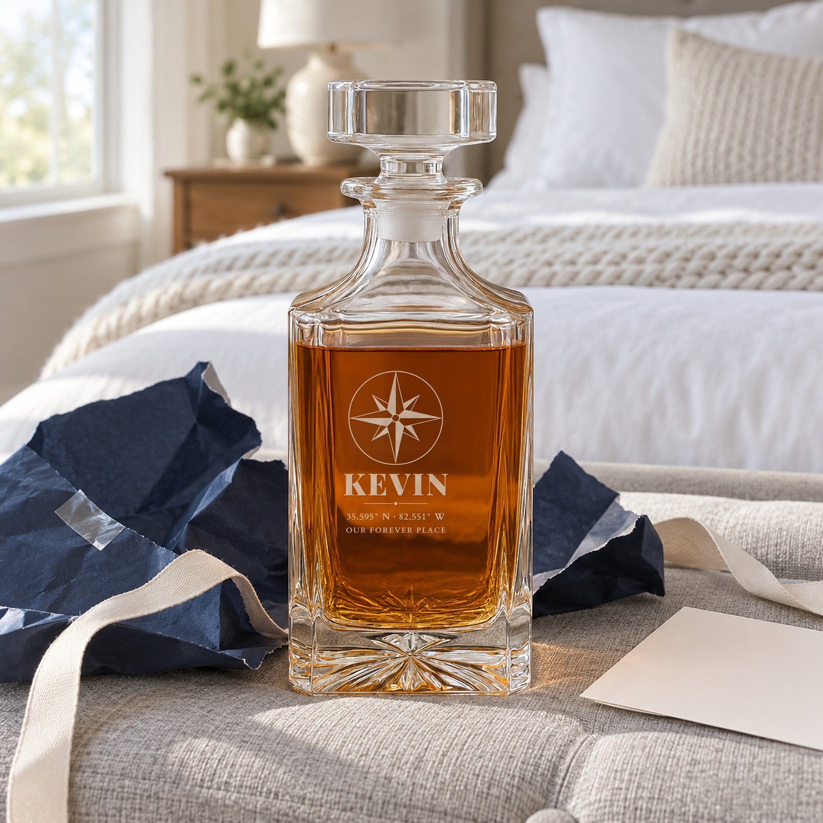 Anniversary gift for him just unwrapped from plain navy paper on a bedroom bench, a whiskey decanter engraved Kevin with Asheville coordinates