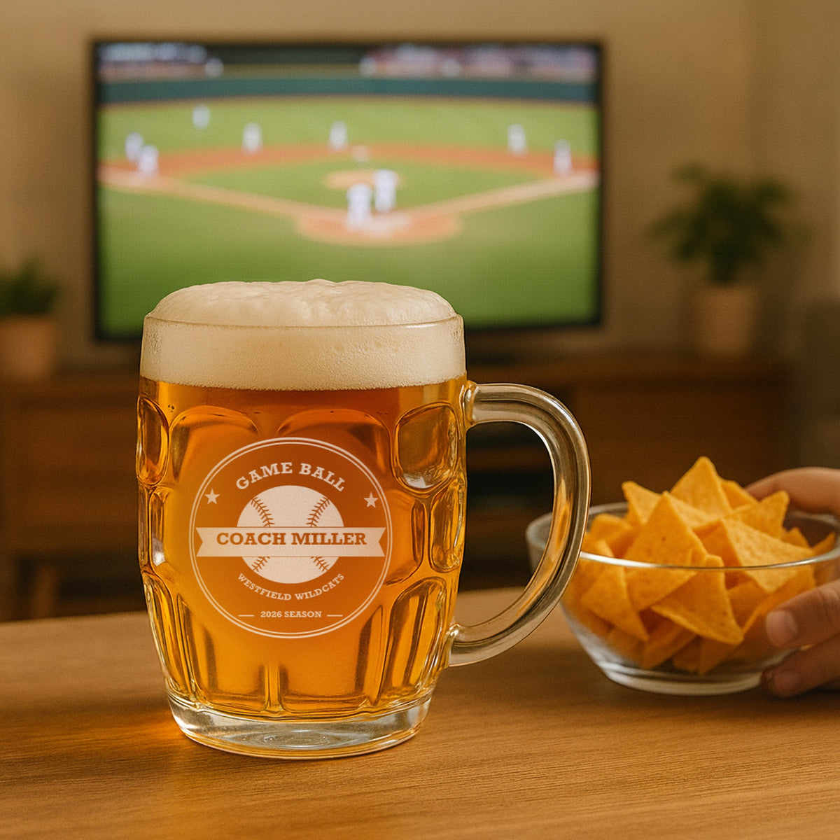 Custom baseball coach beer stein of lager on a living room table beside a bowl of chips, with a baseball game on the TV behind it