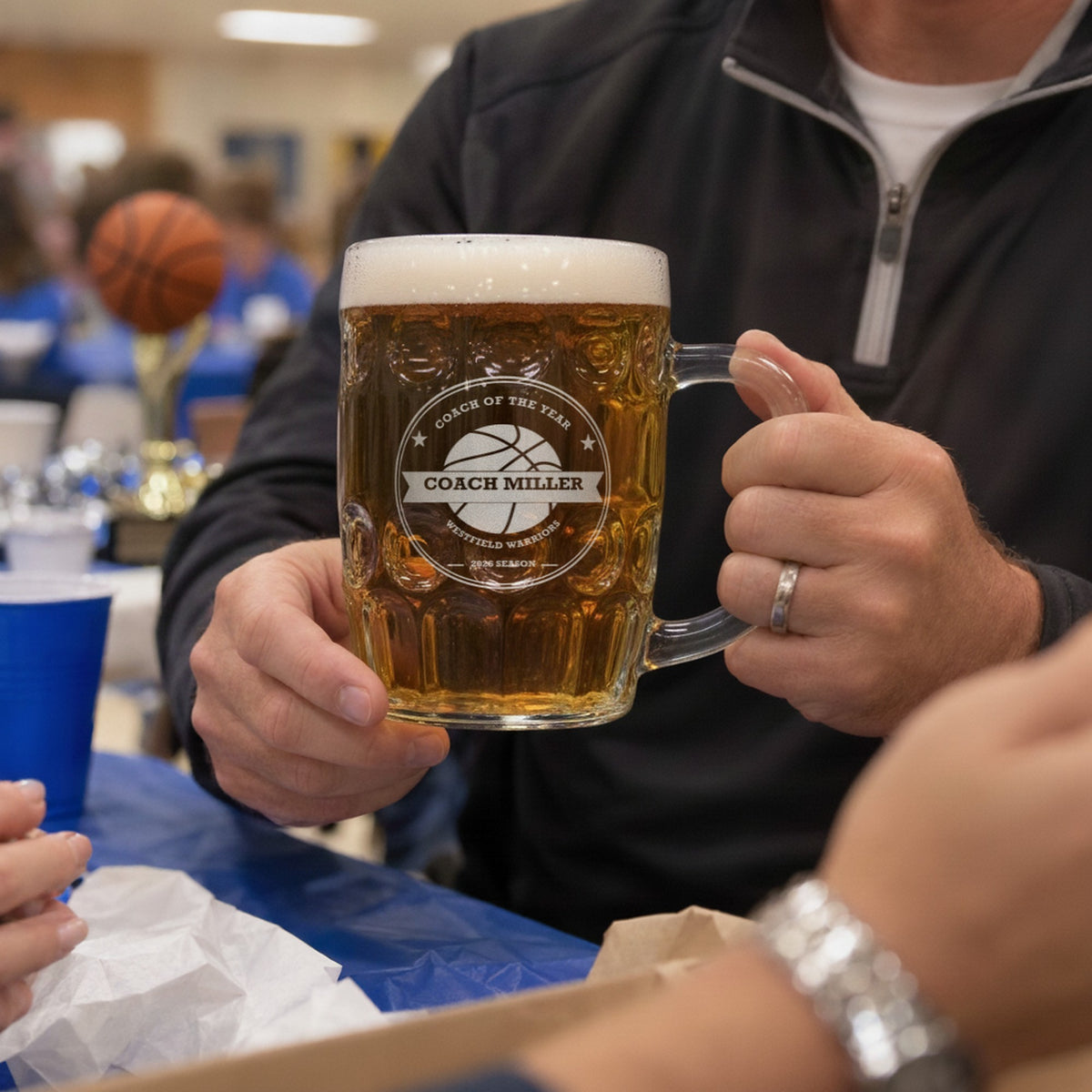 Basketball coach holding the personalized beer stein at an end-of-season team banquet, with a basketball trophy in the background