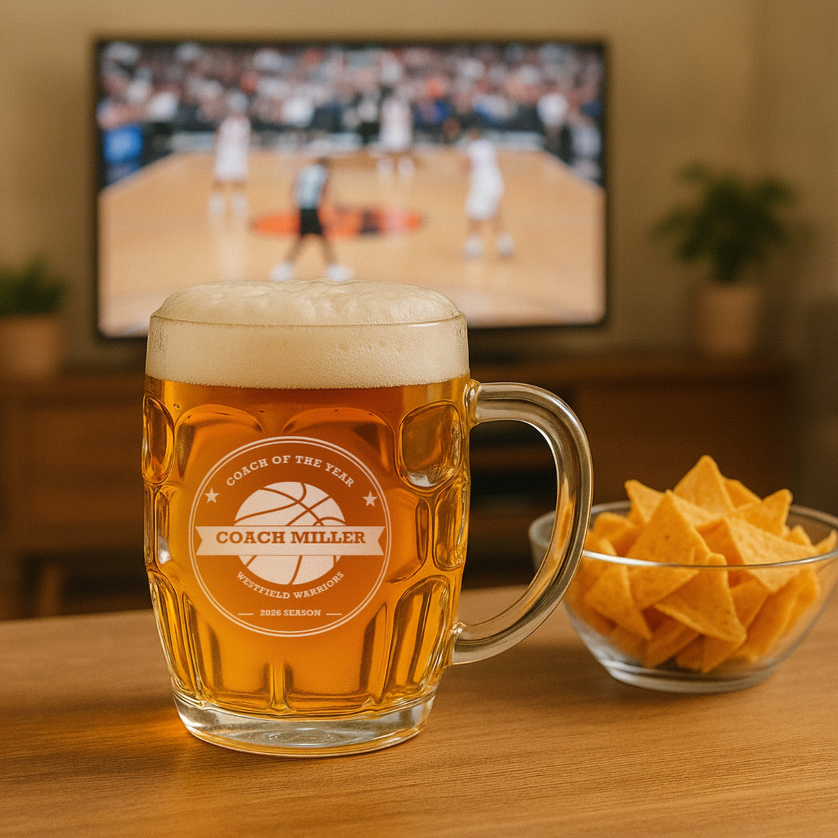 Custom basketball coach beer stein of lager on a living room table beside a bowl of chips, with a basketball game on the TV behind it